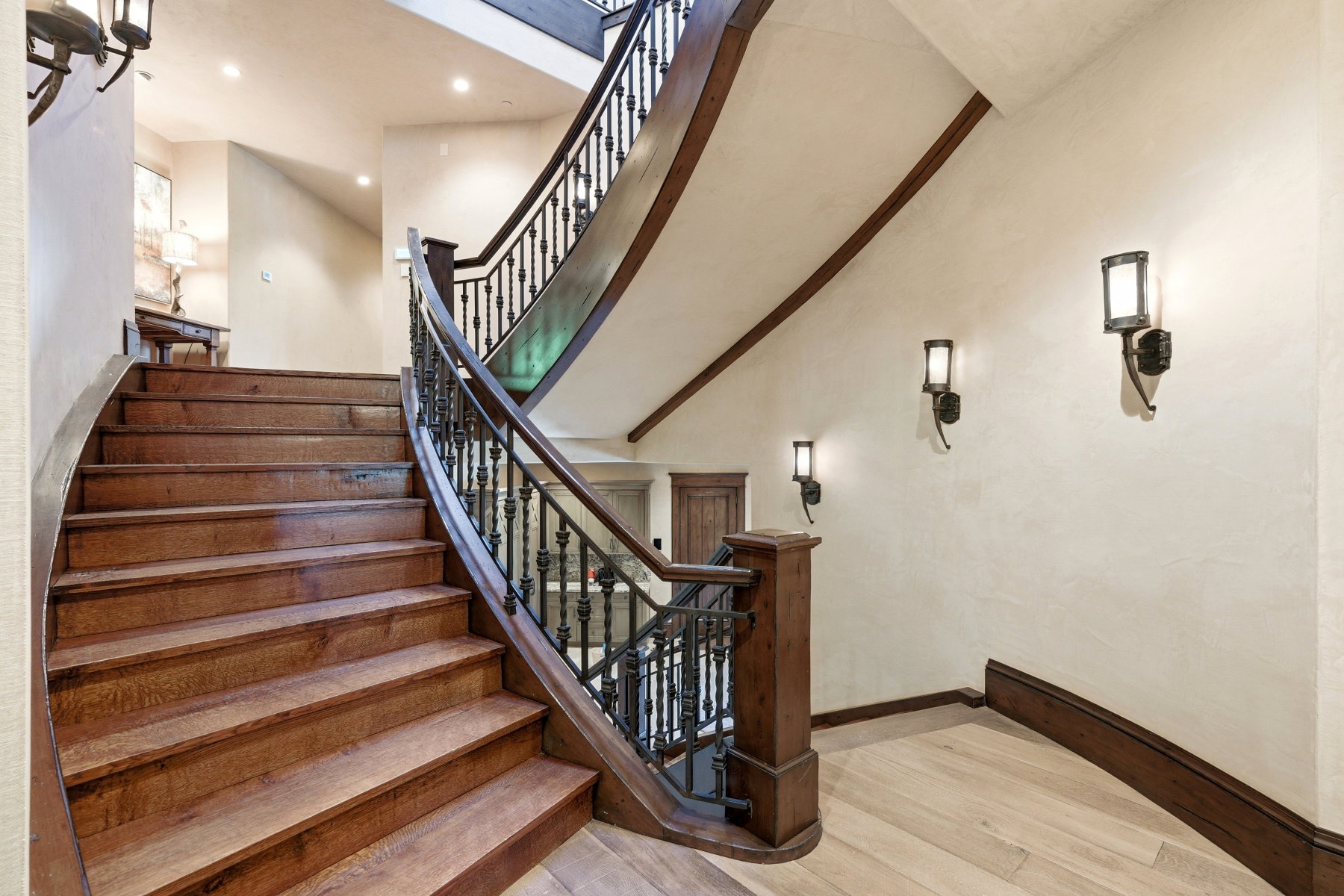 Grand curved staircase featuring wood-finish treads and risers, dark wood handrails, and ornate wrought iron balusters