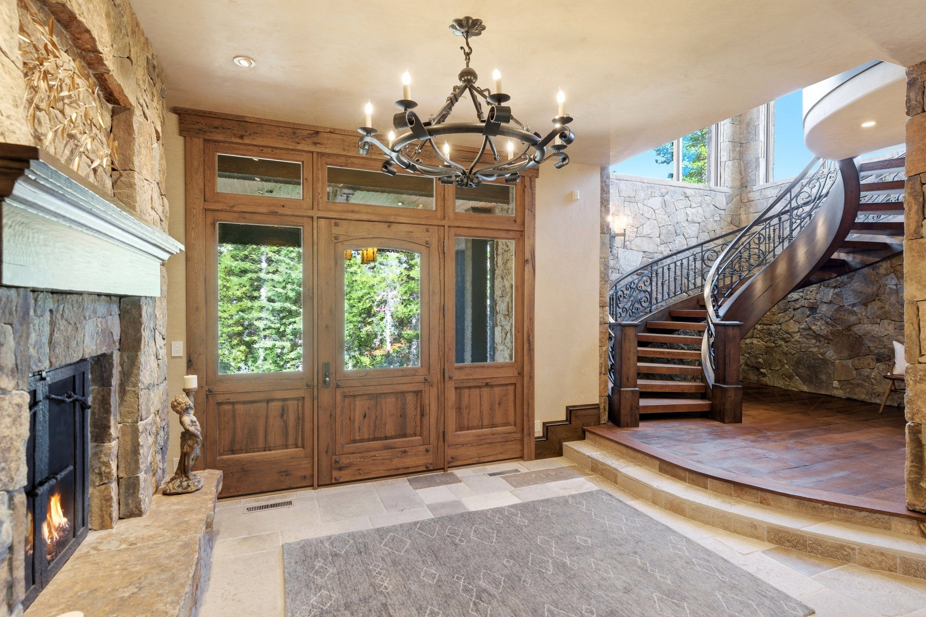 Grand entry featuring a curved staircase with wrought iron railing, stone accent walls, and a stone fireplace with a wood mantel