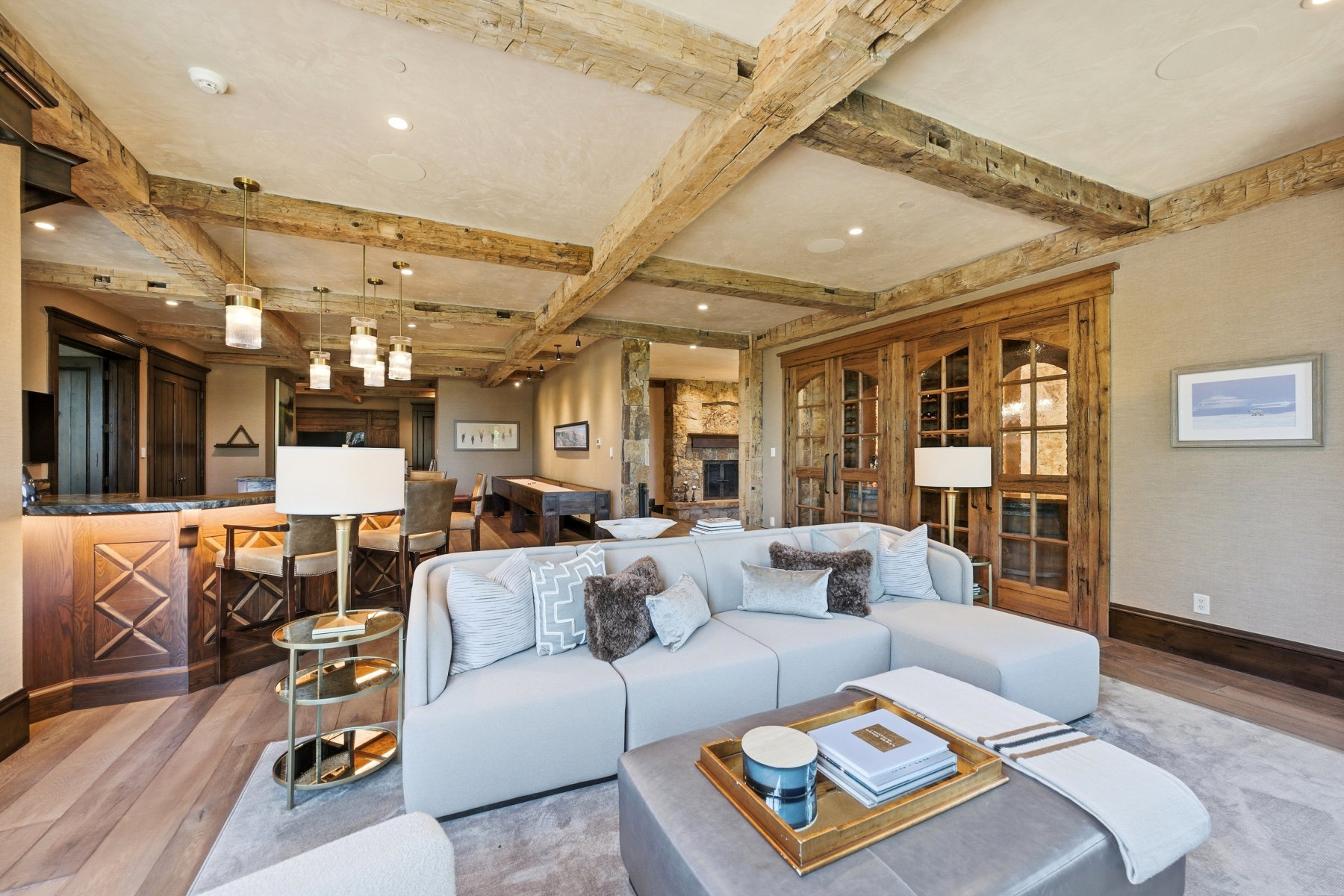 Great room featuring exposed wood beam ceilings, a built-in bar with wood paneling and stone countertop, wood-finish flooring, and a glass-paned wood barn door