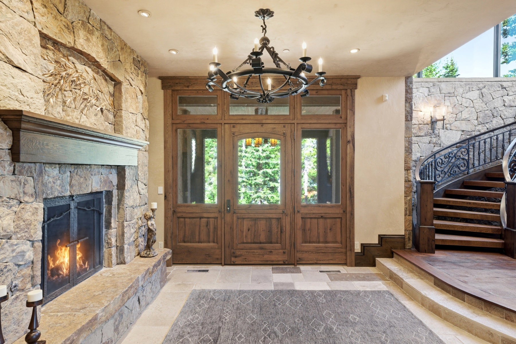 Grand entryway featuring a rustic wood door with side windows, a stone-clad fireplace, and a sweeping wooden staircase with an ornate iron railing