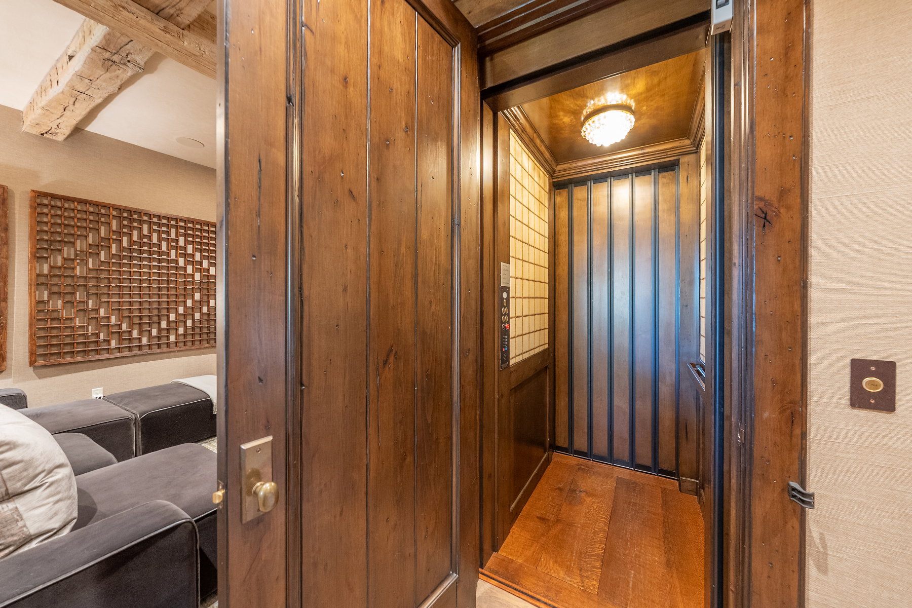 Private interior elevator featuring wood-finish walls and flooring, a decorative cage door, and an ornate ceiling light fixture