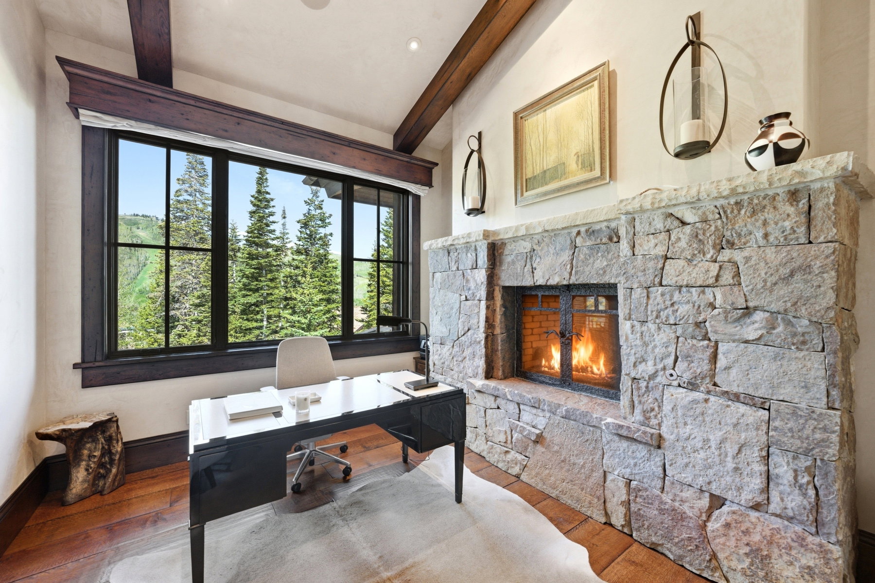 Room featuring a stone fireplace, wood-finish flooring, and exposed ceiling beams