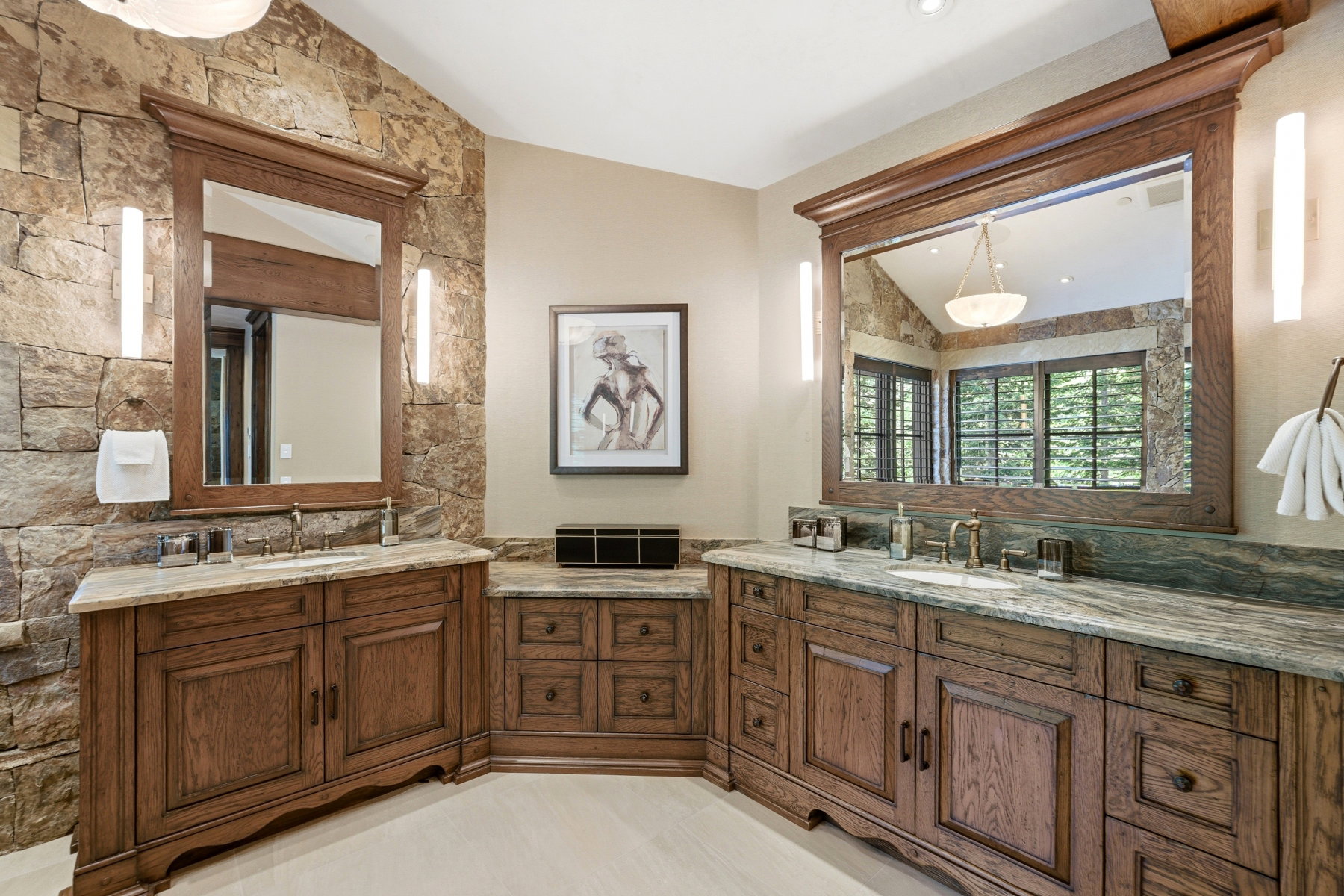 Double vanity featuring custom wood cabinetry, stone countertops, integrated sinks, and wall-mounted sconces