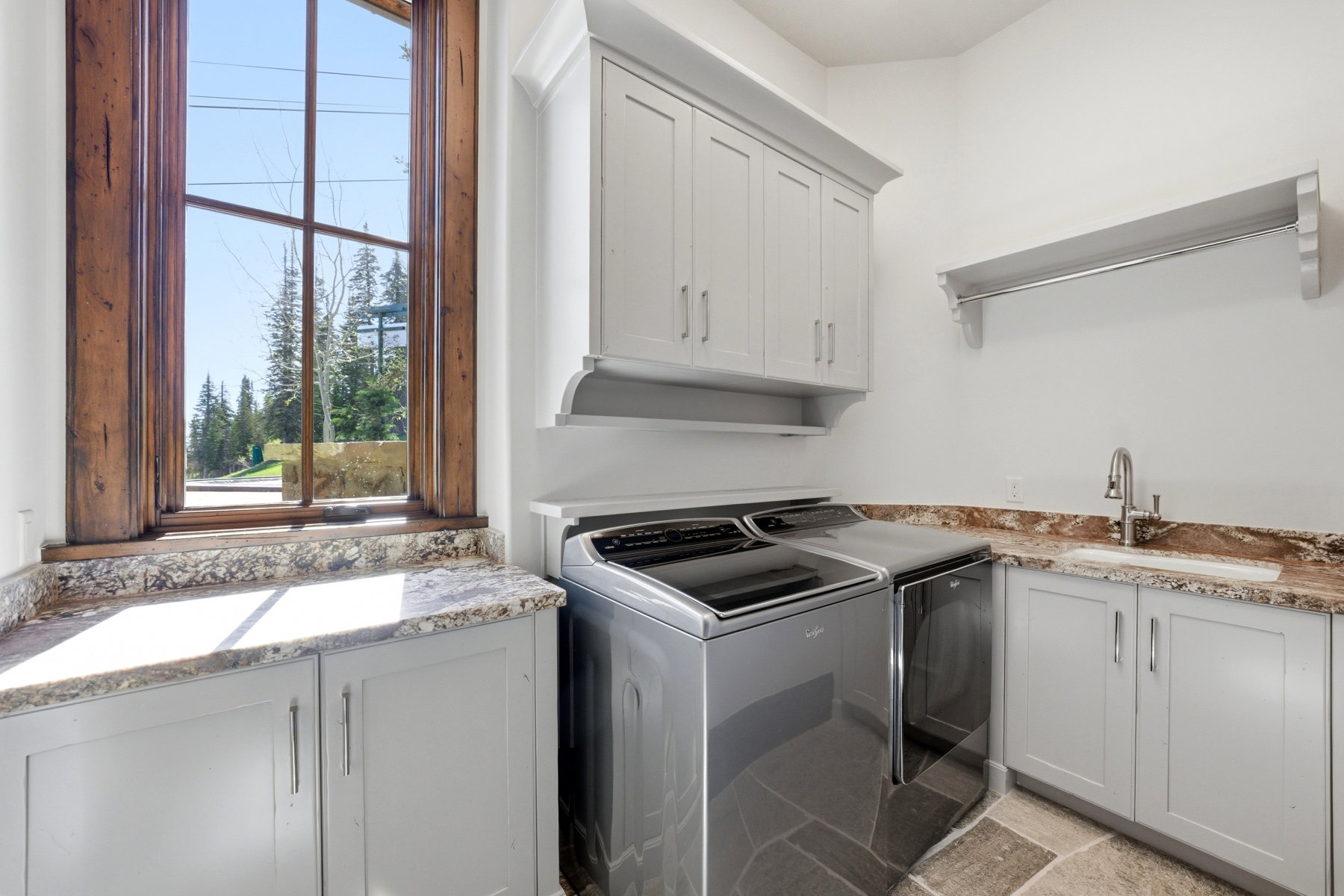 Utility room featuring light grey cabinetry, stone-finish flooring, a built-in sink with a gooseneck faucet, and extensive counter space with a stone-look finish
