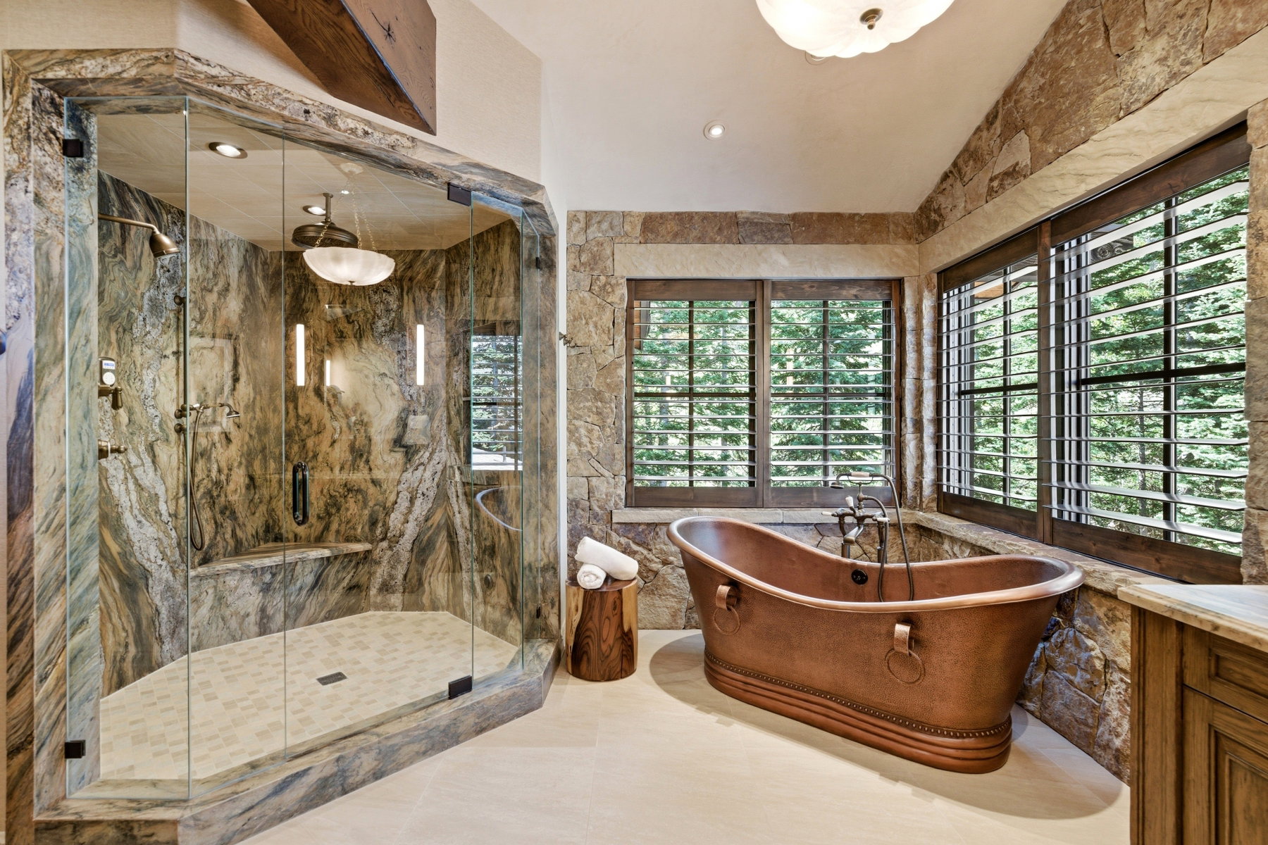 Stone-clad bathroom featuring a freestanding copper soaking tub and a glass-enclosed shower with a built-in bench