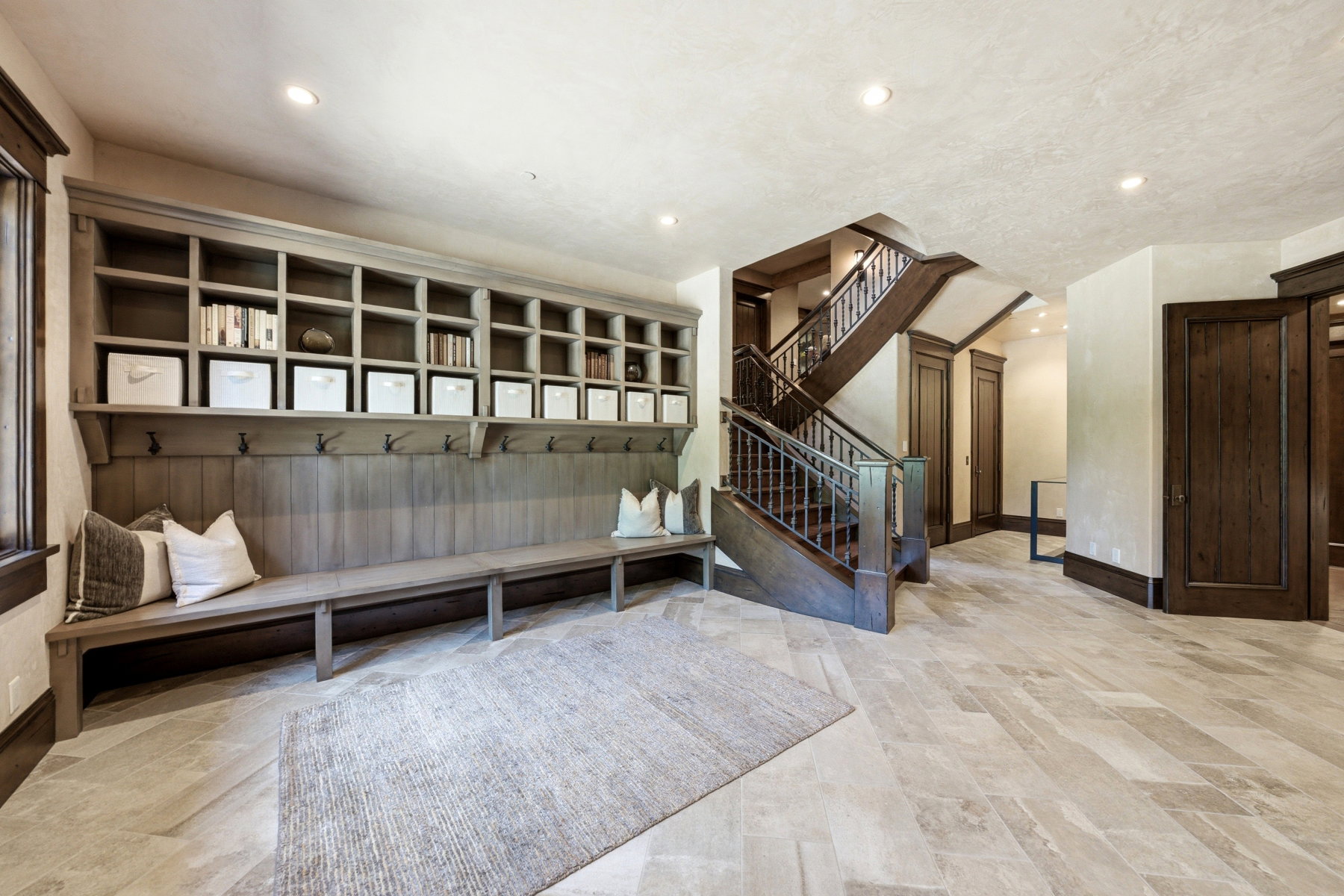 Spacious entryway featuring light-toned tile flooring, a built-in wood bench with integrated shelving and coat hooks, and a grand staircase with dark wood banisters
