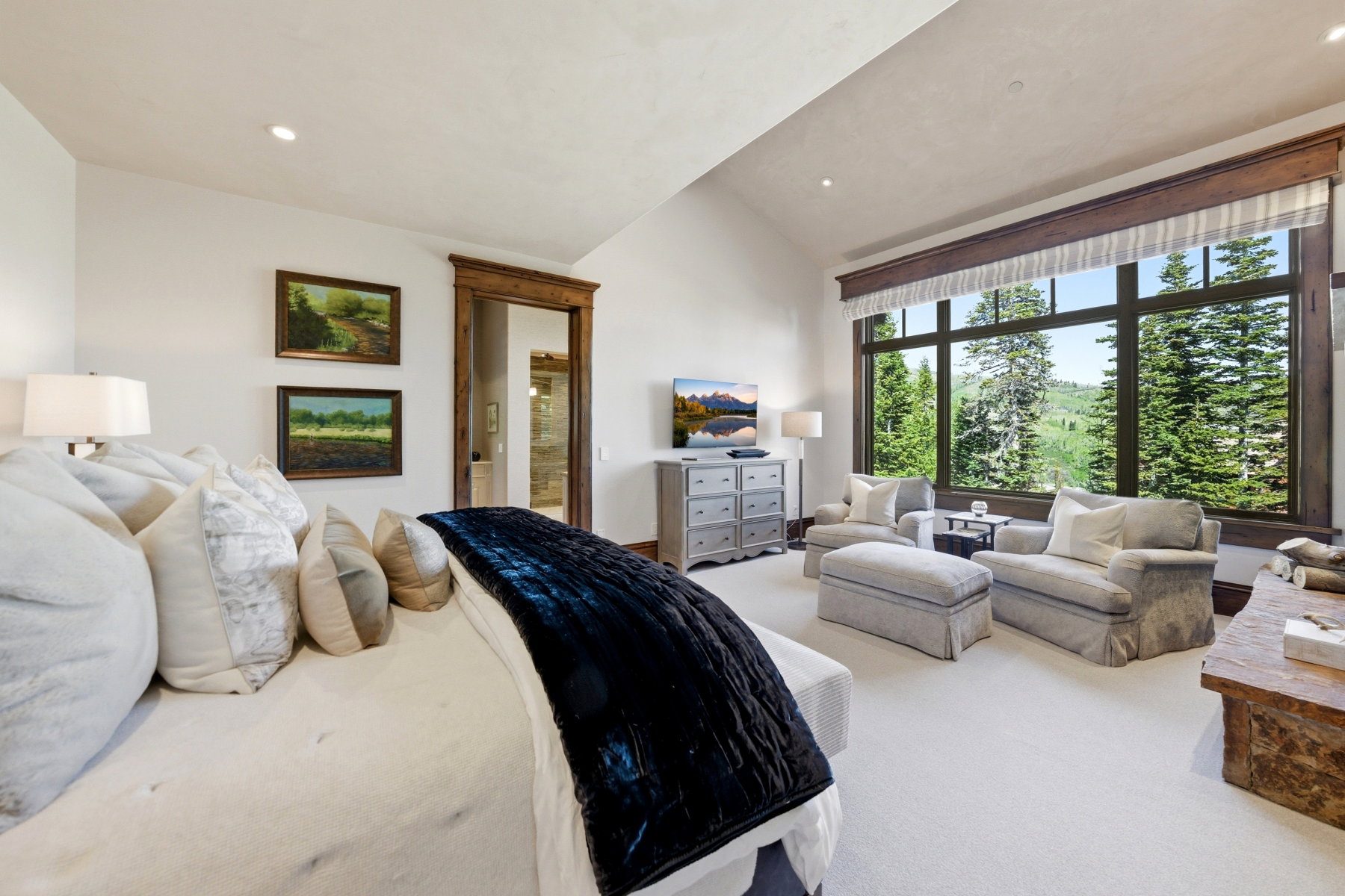 Spacious room featuring vaulted ceilings, recessed lighting, and a large window wall showcasing evergreen trees