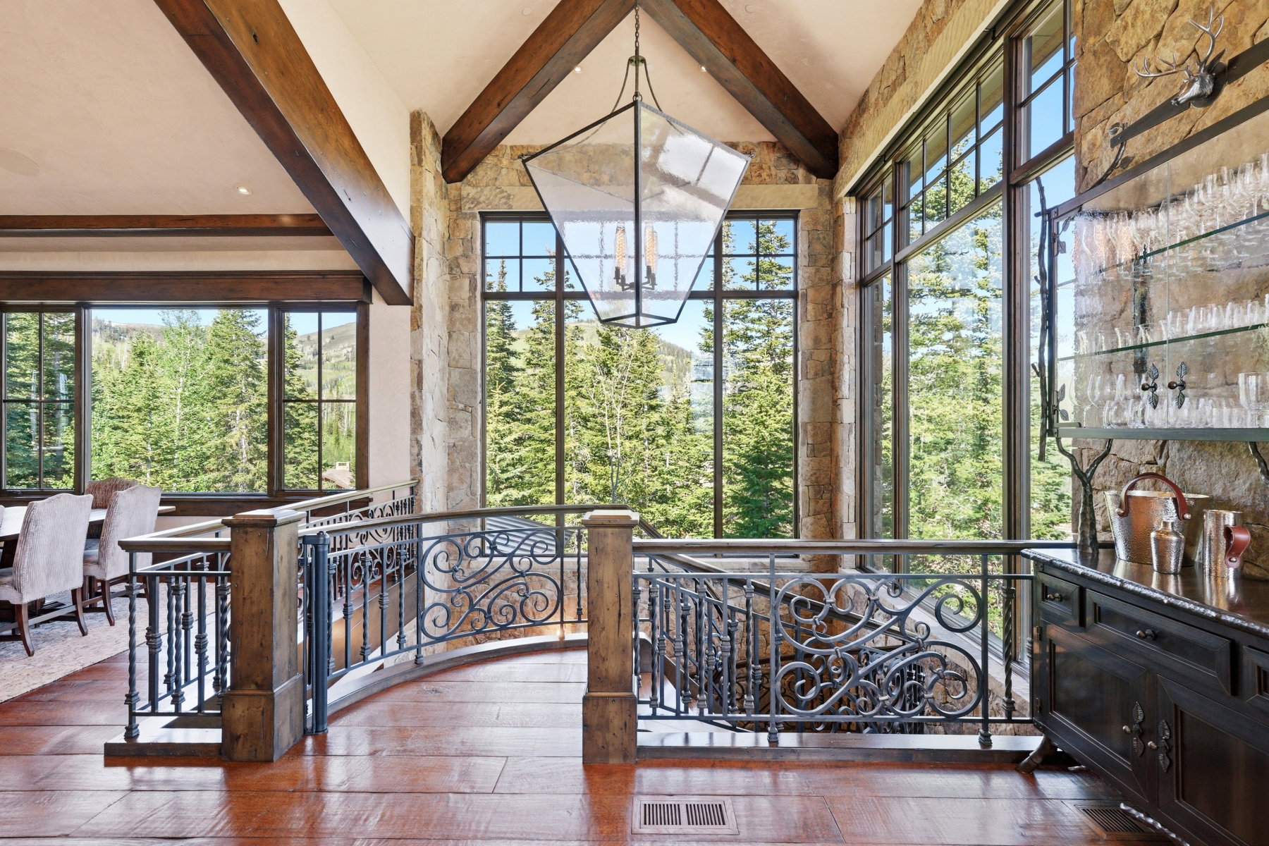 Vaulted ceilings with exposed timber beams define this interior space, featuring a curved wrought iron railing and wood-finish flooring