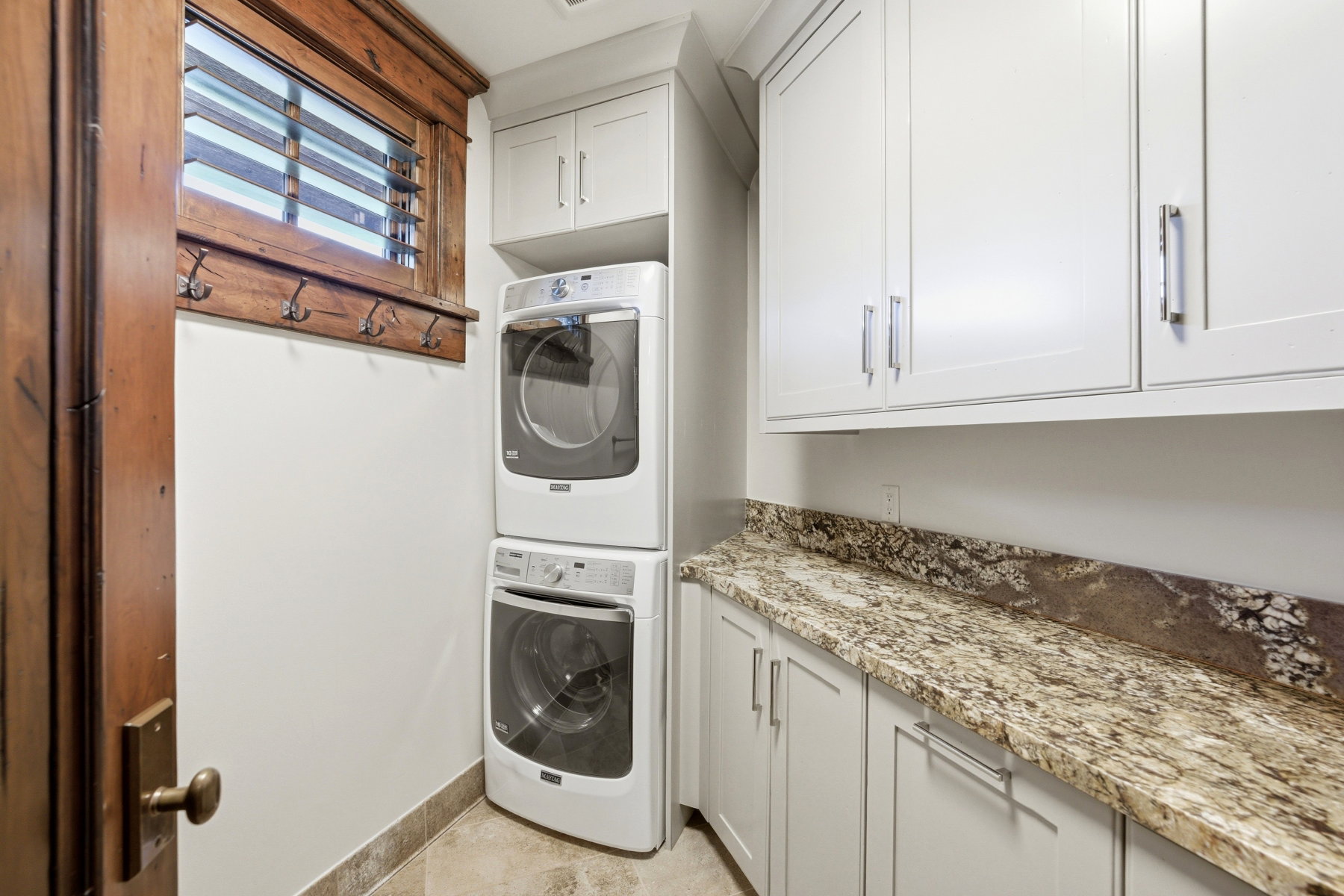 Laundry area featuring a stacked washer and dryer, light-toned cabinetry, granite-finish countertop, and tile flooring