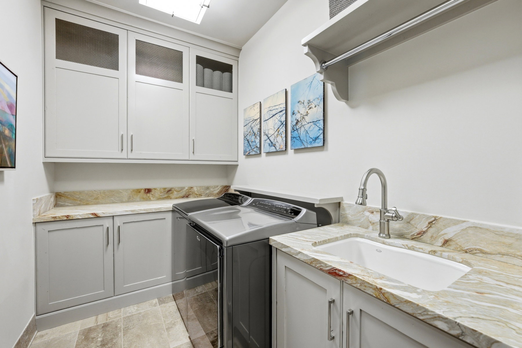 Laundry area featuring light gray cabinetry, patterned stone countertops, an undermount sink with a pull-down faucet, and tiled flooring