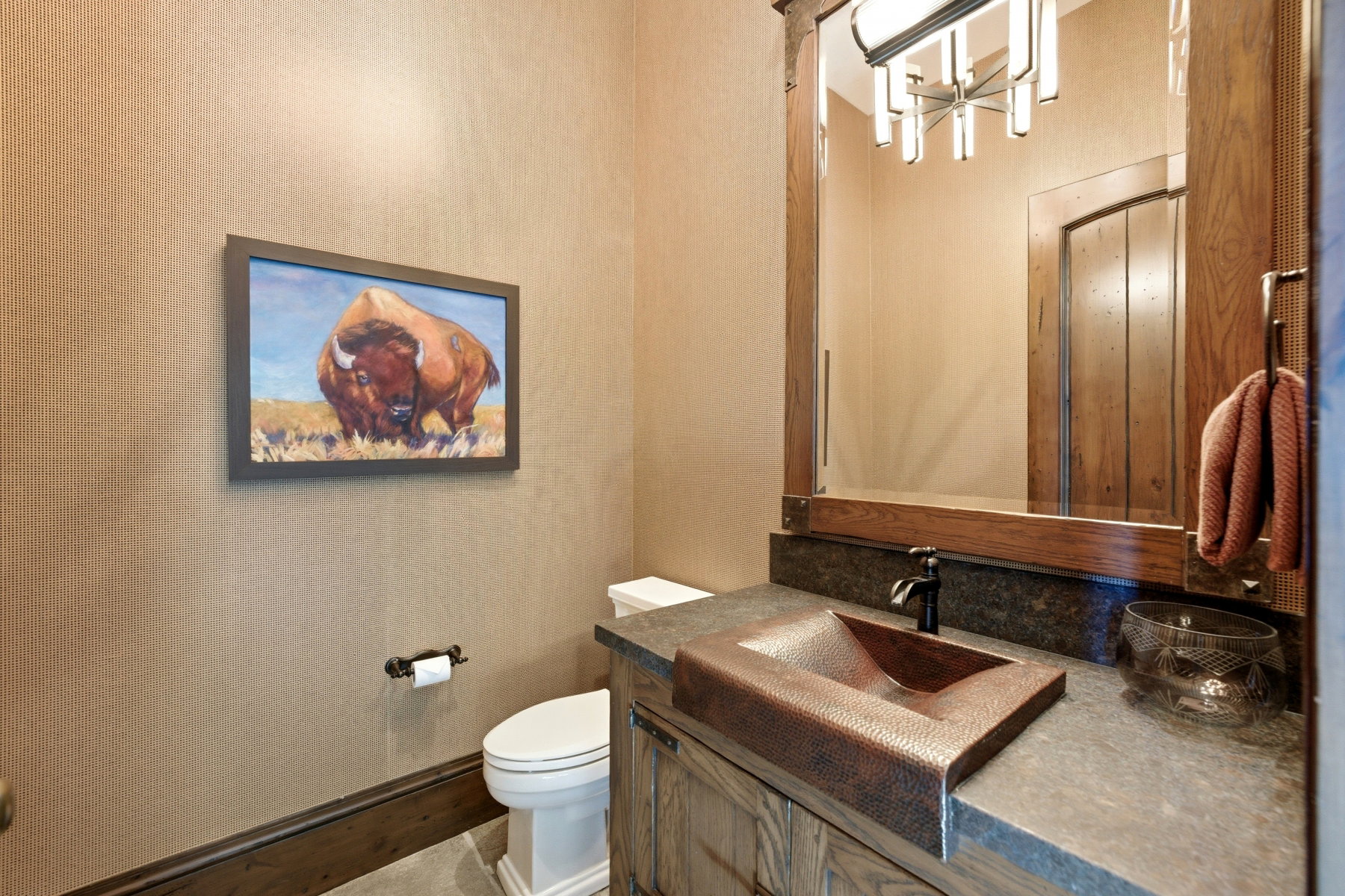 Powder room featuring a hammered copper vessel sink, stone countertop, custom wood vanity, and a framed wood mirror