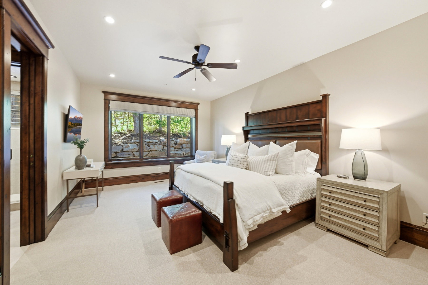 Spacious bedroom featuring light-toned carpeting and wood-trimmed windows overlooking natural surroundings