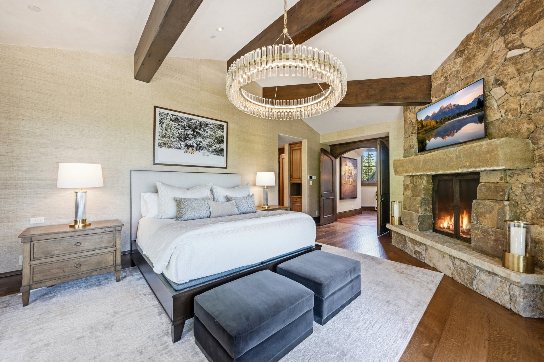 Vaulted ceiling with exposed wood beams, stone fireplace with hearth, and wood-finish flooring