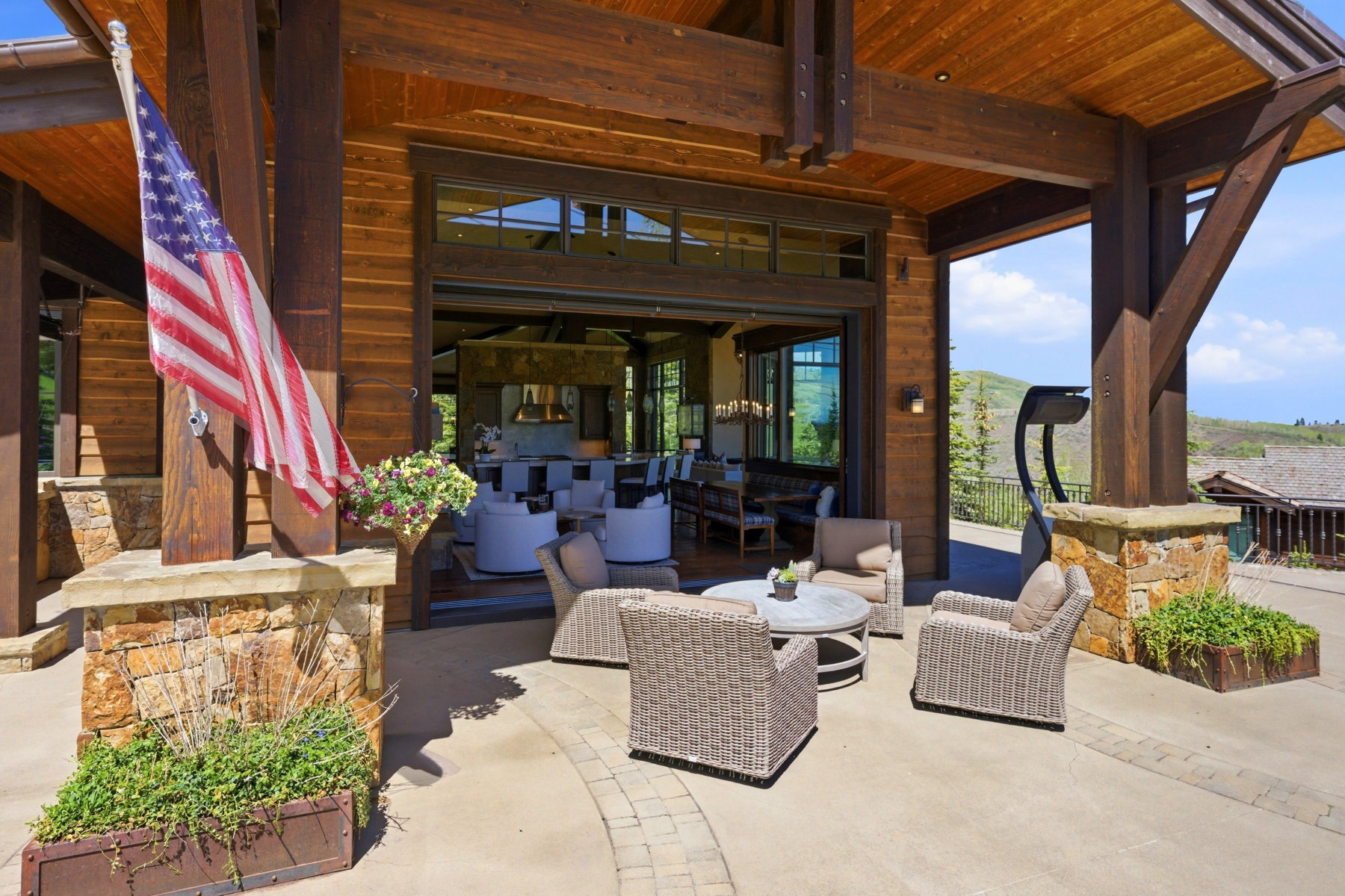 Spacious covered patio featuring stone-clad pillars, exposed wood beams, and large sliding glass doors