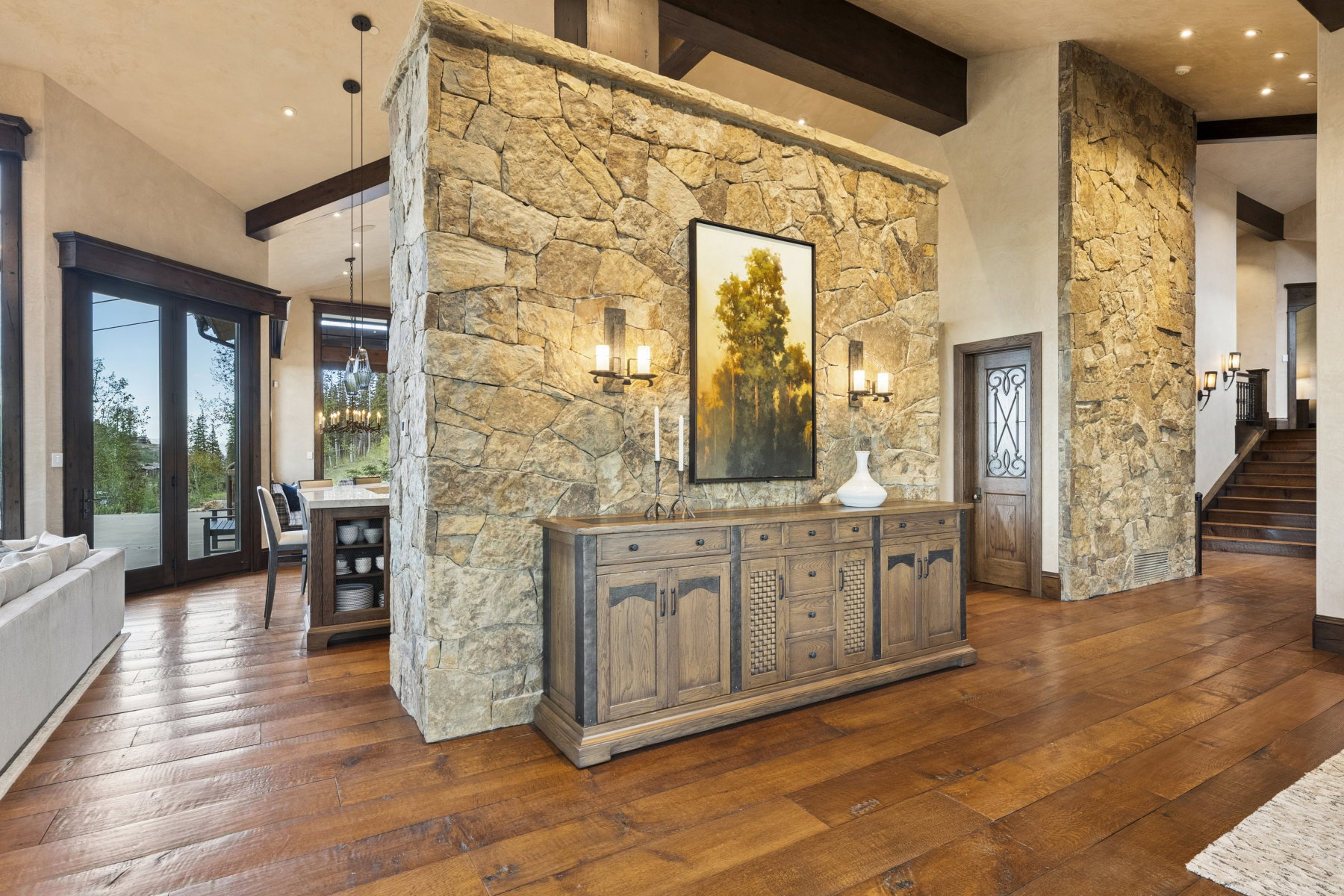 Expansive interior featuring stone accent walls, vaulted ceilings with exposed wood beams, and wide plank wood-finish flooring