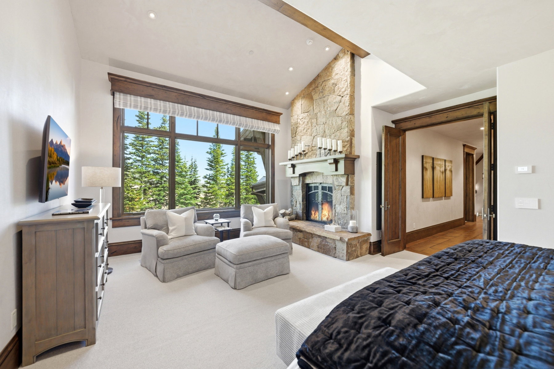 Vaulted ceiling room featuring a natural stone fireplace with a substantial hearth, large picture windows, wood-finish trim, and recessed lighting