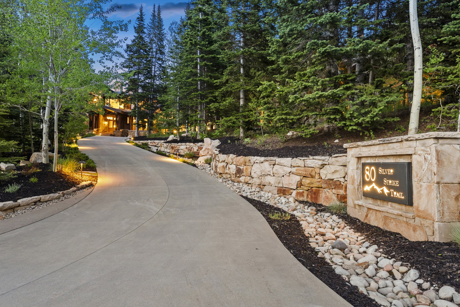 Curved concrete driveway with integrated landscape lighting, complemented by a stone retaining wall and an illuminated address marker
