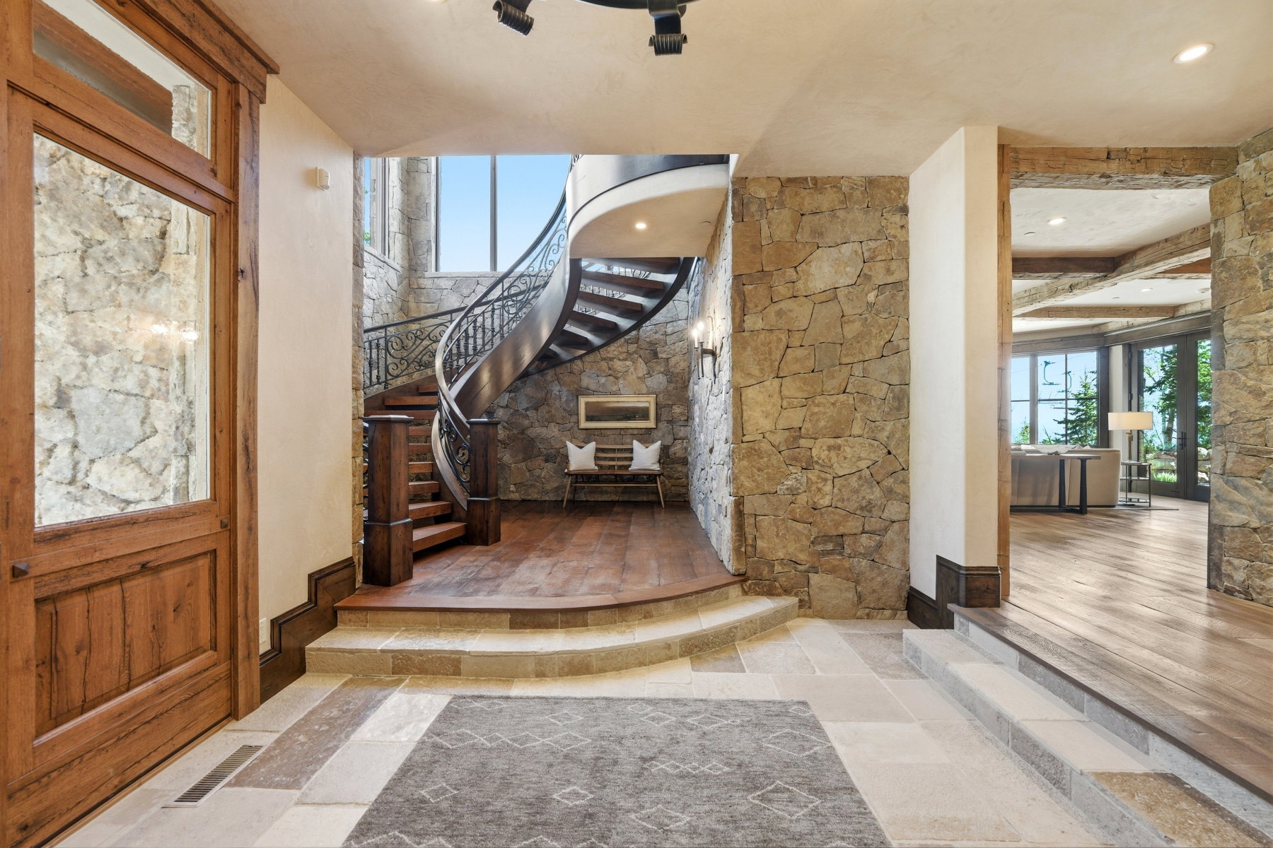 Grand entryway featuring a custom spiral staircase with ornate iron railings, natural stone wall finishes, and wood-finish flooring