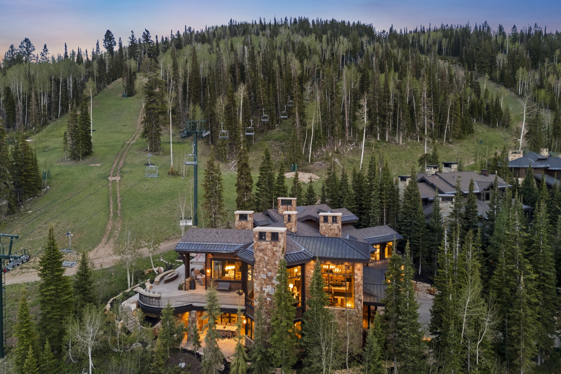 Expansive mountain estate featuring multiple stone chimneys, a dark metal roof, and large picture windows