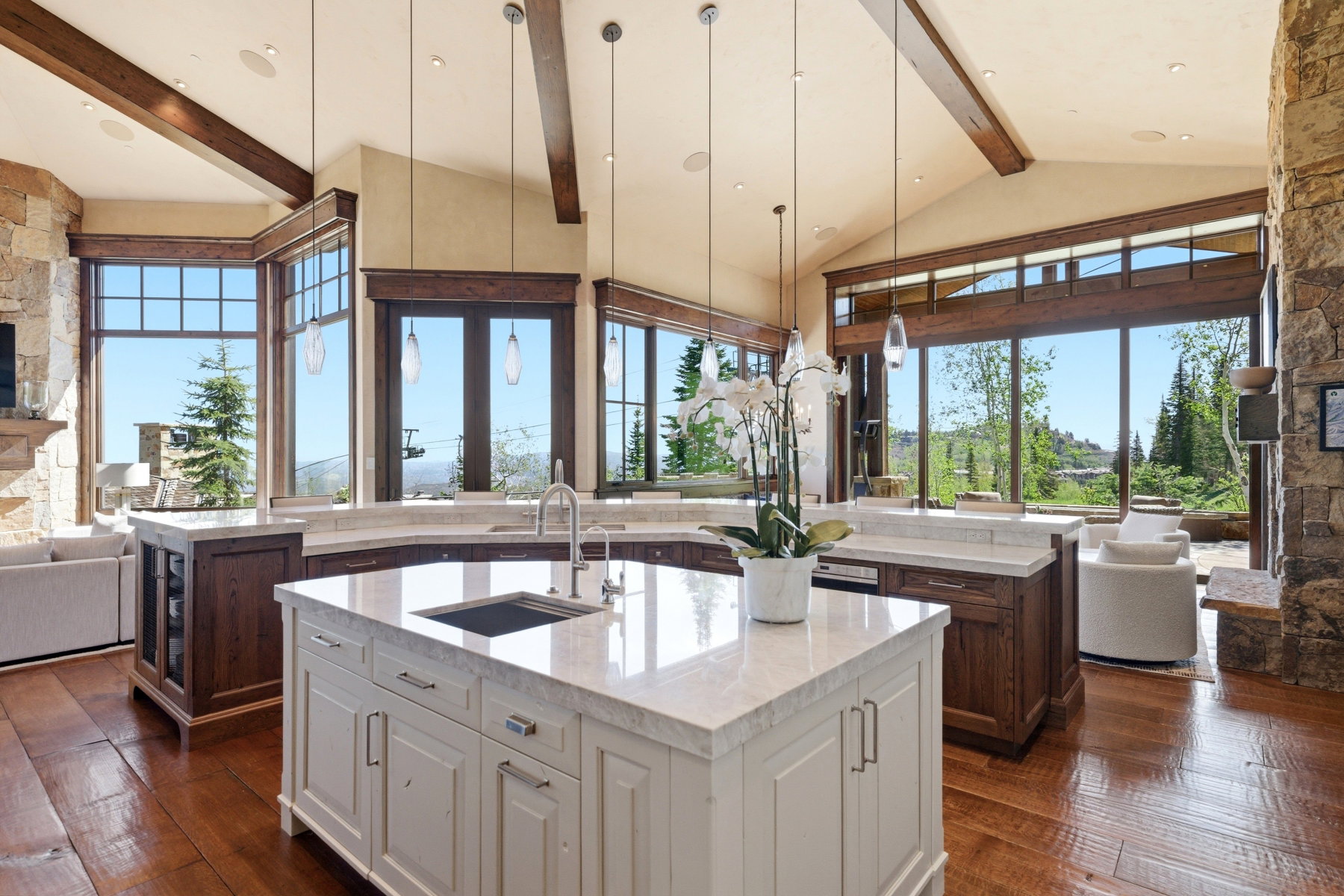 Gourmet kitchen featuring a central island with an undermount sink, stone countertops, exposed wood beams, and extensive natural light through large windows