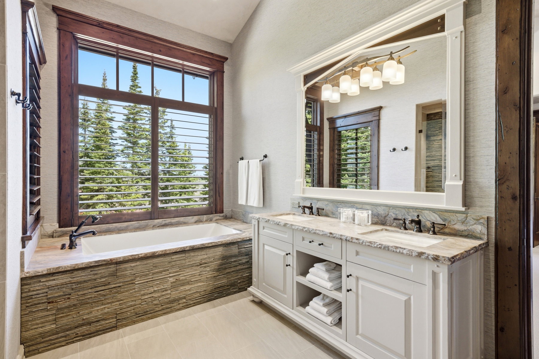 Bathroom featuring a built-in soaking tub with stone tile surround and a large window with wood plantation shutters