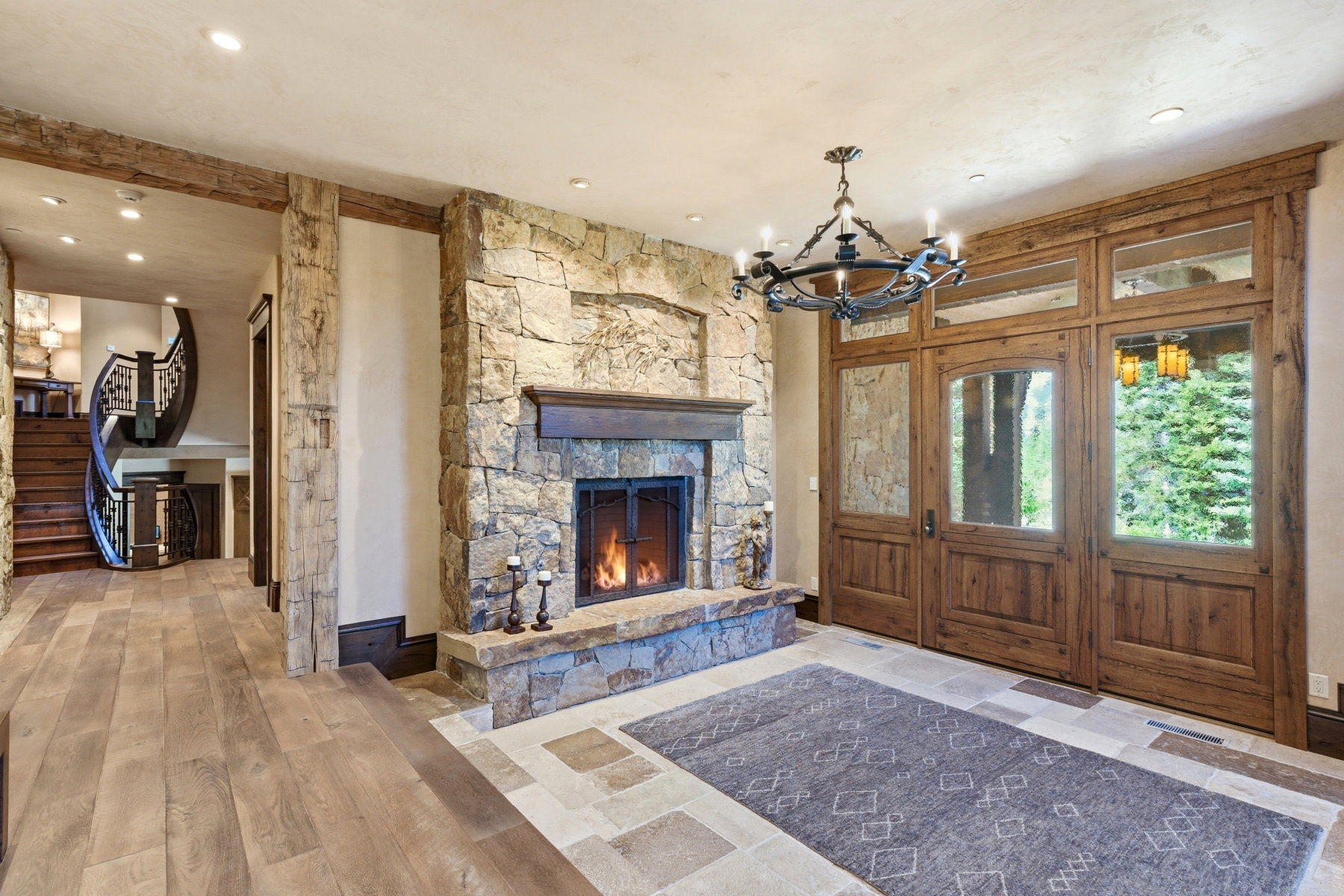 Stone fireplace with a mantle and hearth, wood-finish flooring, exposed wood beams, and a wrought iron chandelier