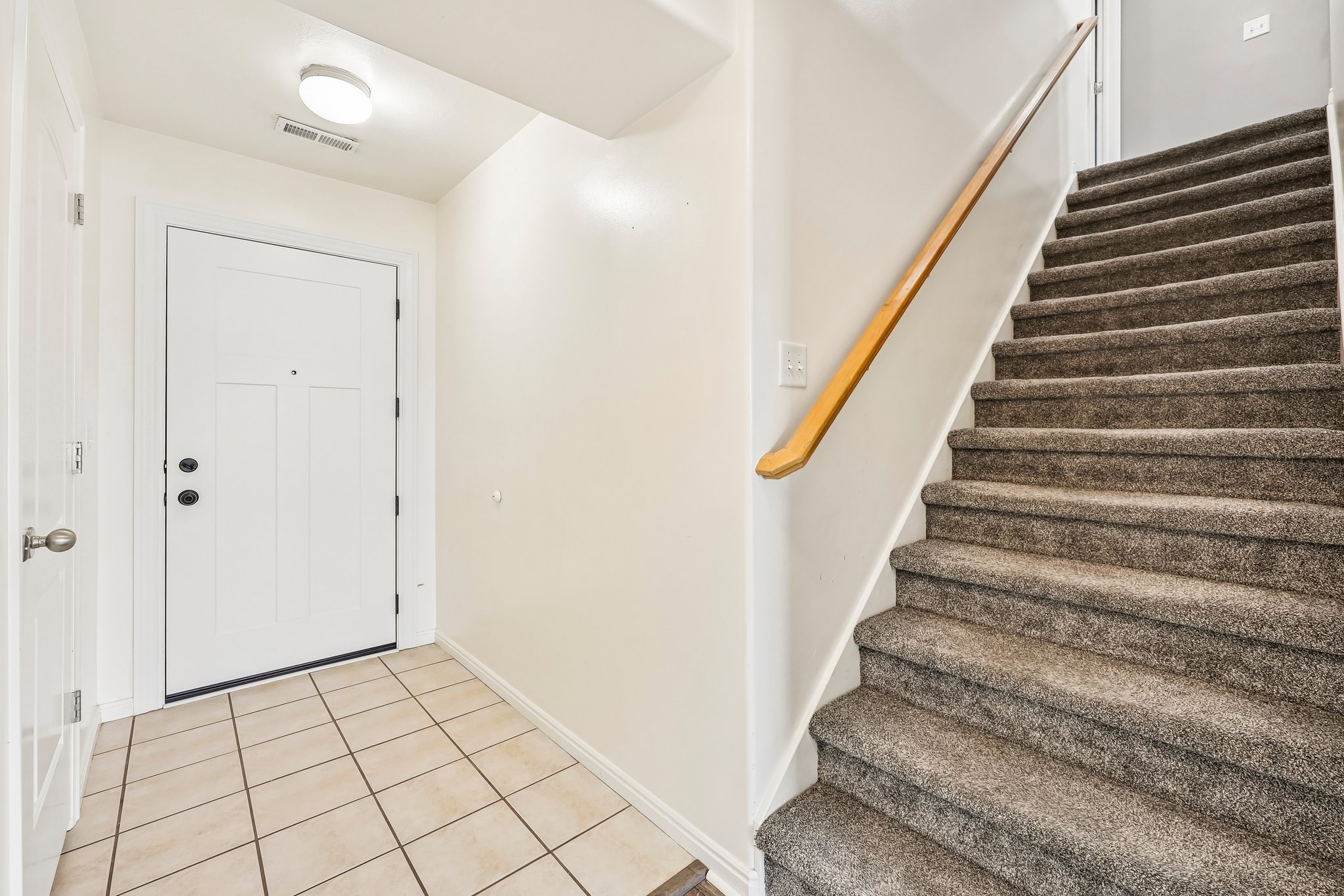 Entryway featuring a white paneled door with dark hardware, square tile flooring, and a carpeted staircase with a wood handrail
