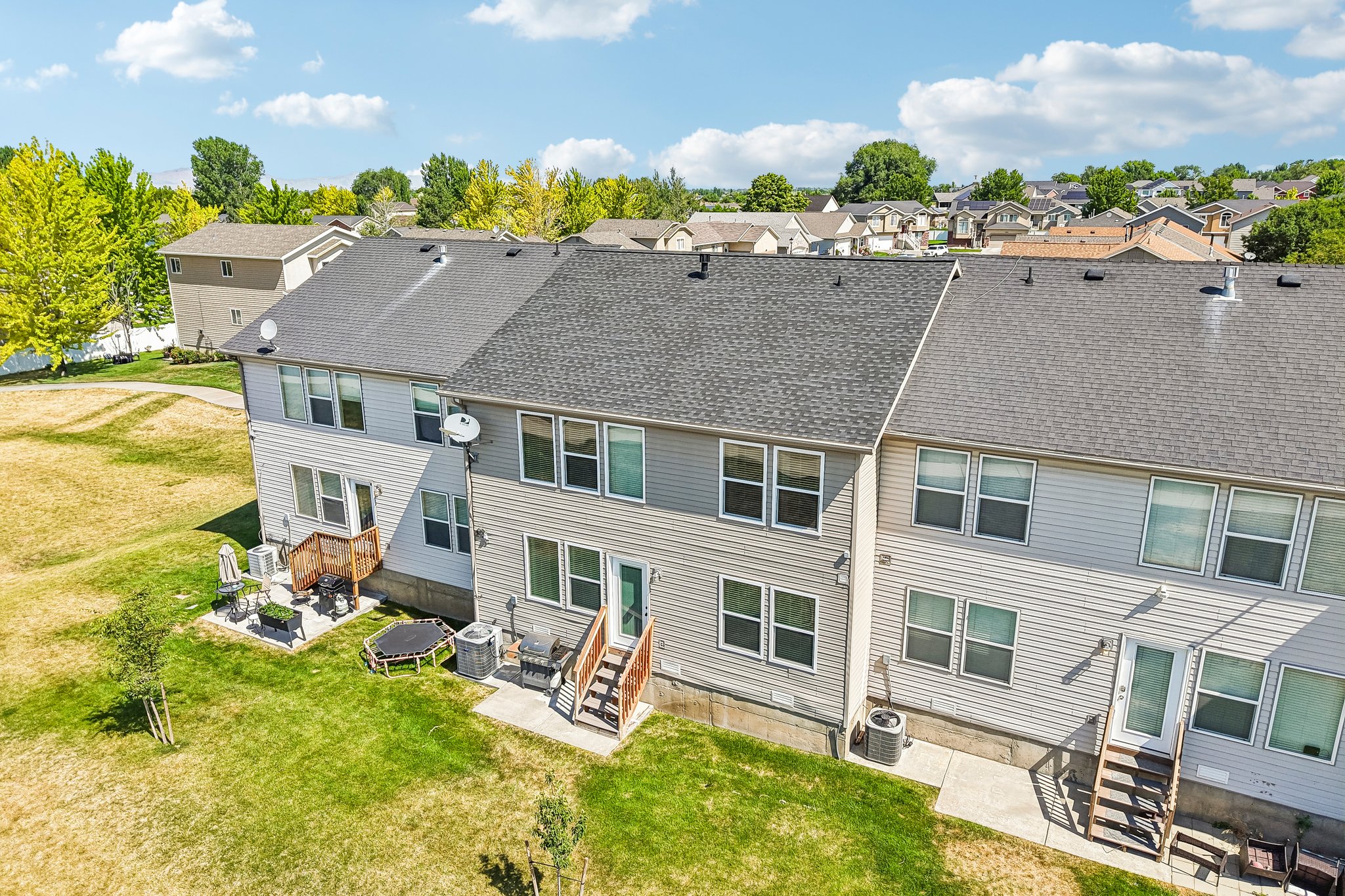 Rear exterior of a multi-unit property featuring light gray horizontal siding and individual concrete patios