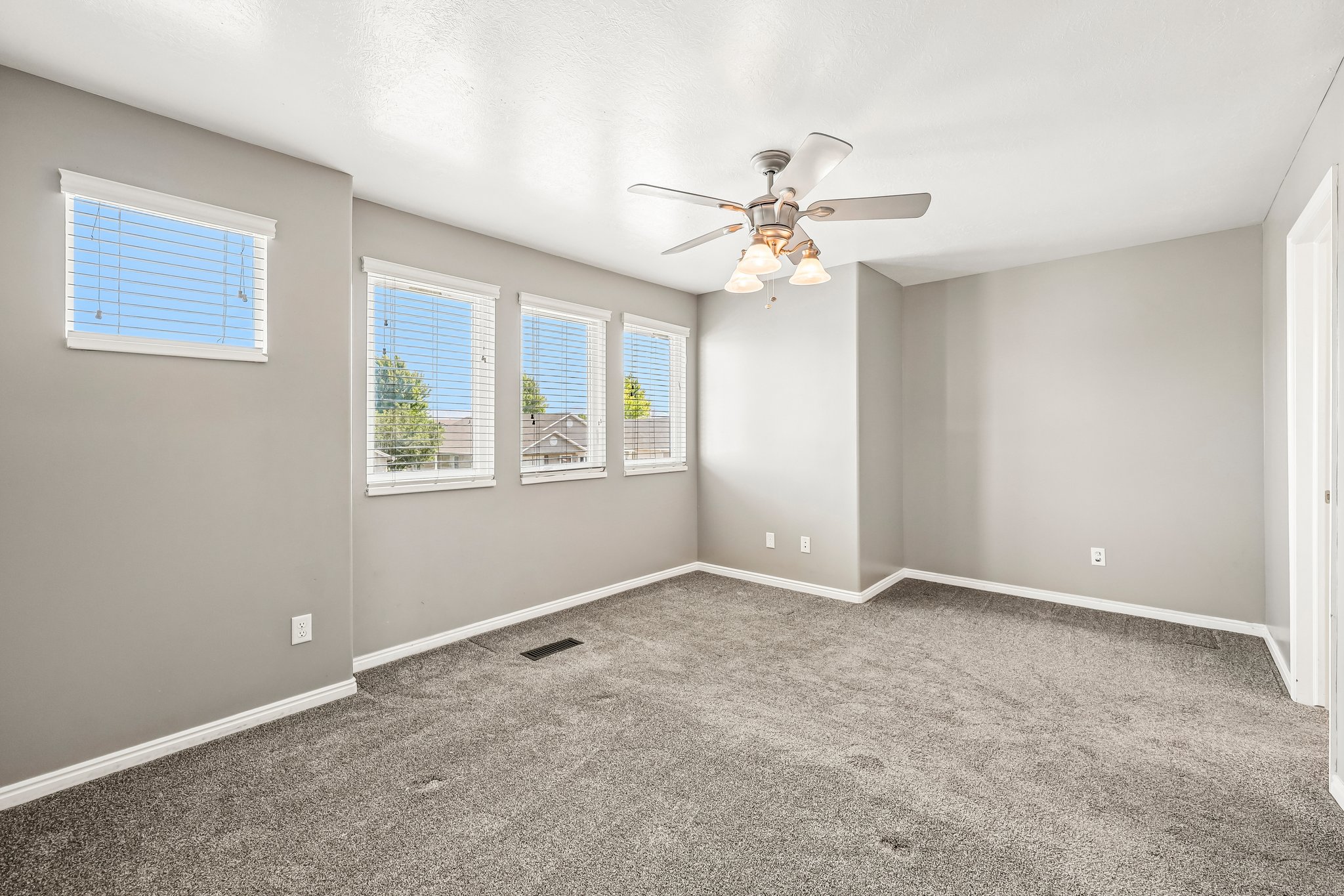 Expansive room featuring plush grey carpeting, light grey wall paint, and multiple windows with blinds