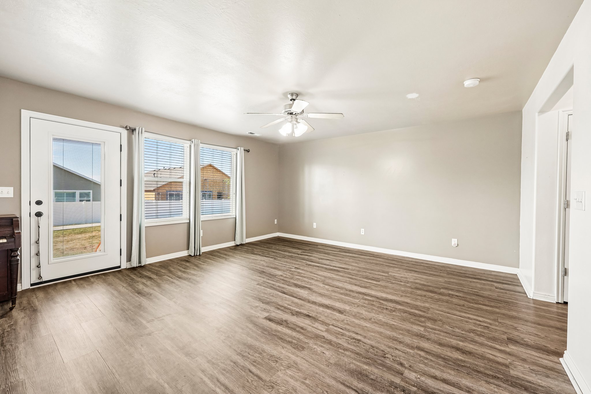 Spacious room featuring wood-finish flooring, light gray wall tones, and a ceiling fan with integrated lighting