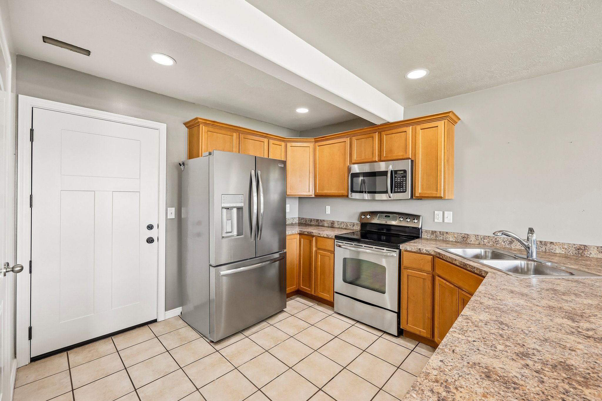 Kitchen featuring stainless steel appliances, light wood cabinetry, a double basin sink, laminate countertops, and square tile flooring