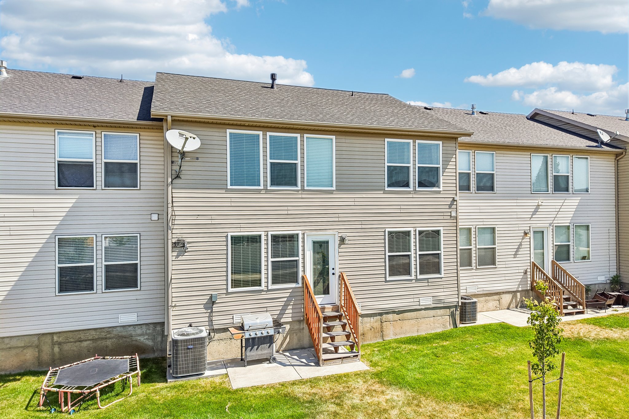 Rear exterior featuring light-colored siding, multiple windows, a ground-level patio, and wood stairs leading to an upper-level door