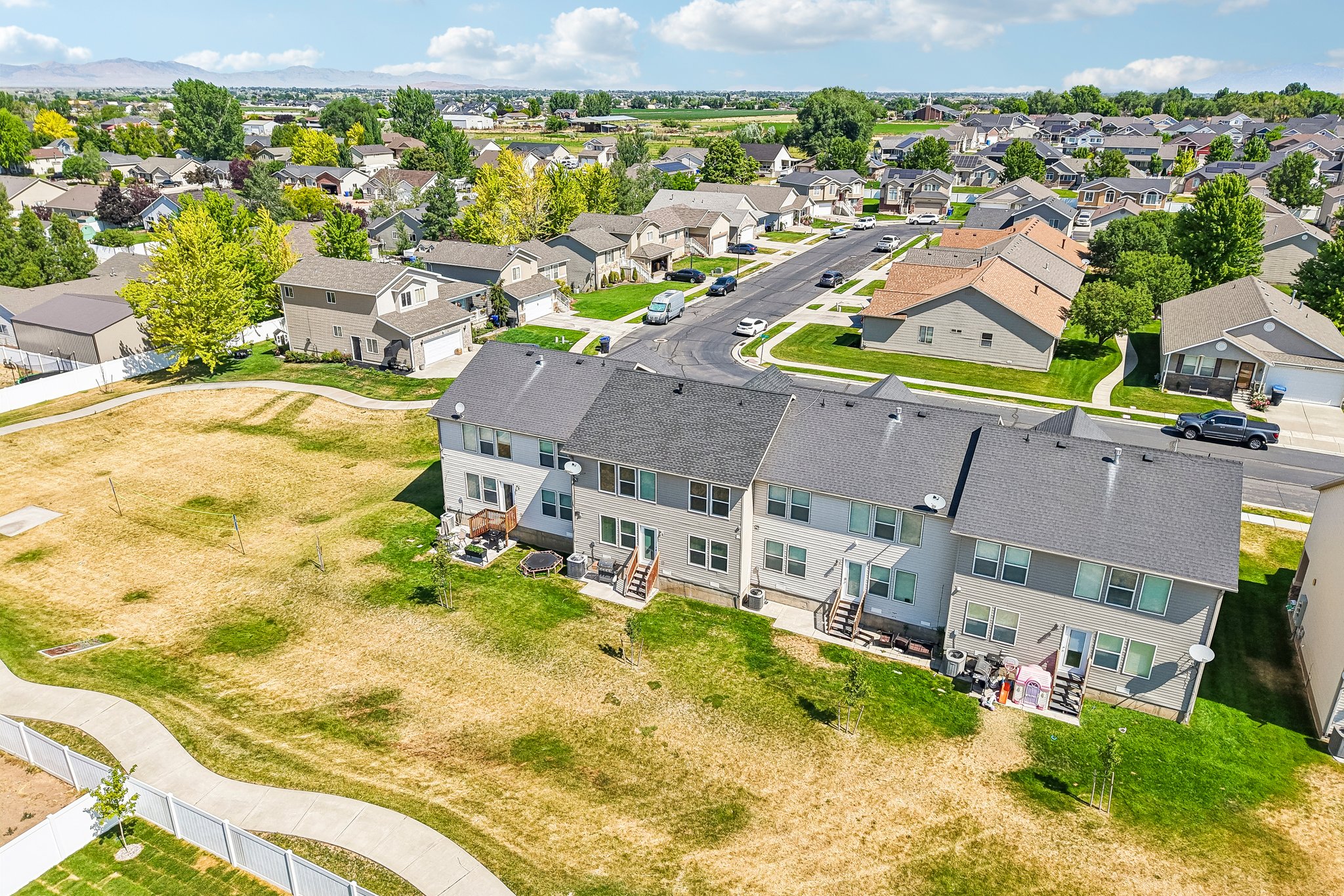 Rear exterior of a multi-story townhome featuring a private deck, ground-level patio, and a grass lawn