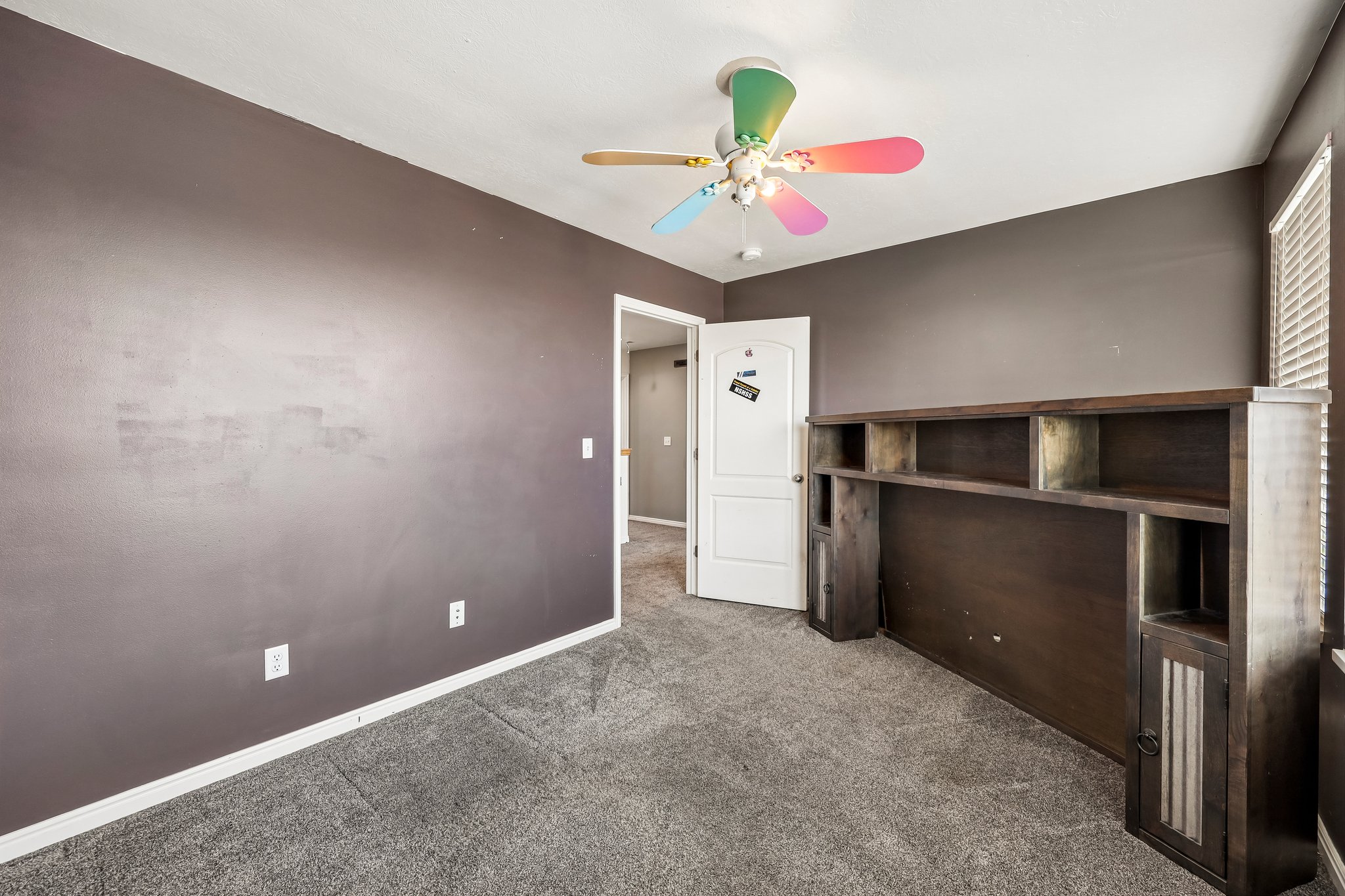 Carpeted room with dark gray walls and a ceiling fan with colorful blades