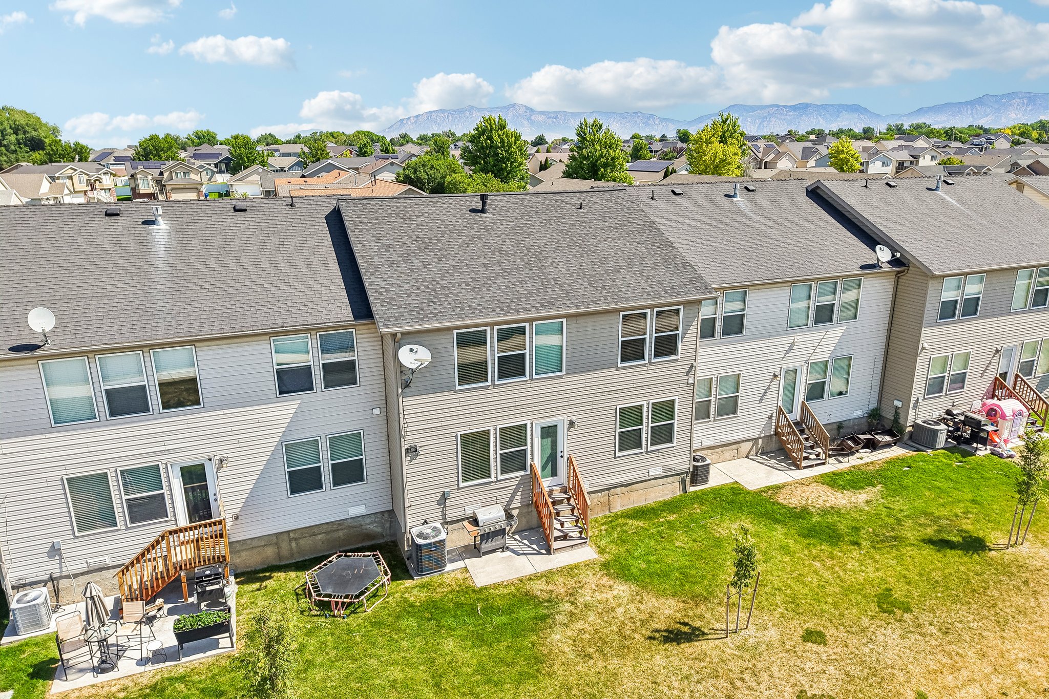 Townhome exterior featuring horizontal siding, a gray shingle roof, multiple windows, a rear deck with wooden steps, and a grass yard