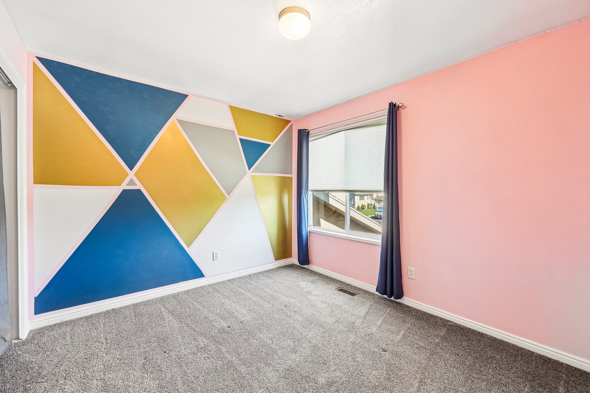 Room featuring a geometric accent wall with blue, gold, and white tones, complemented by soft pink walls