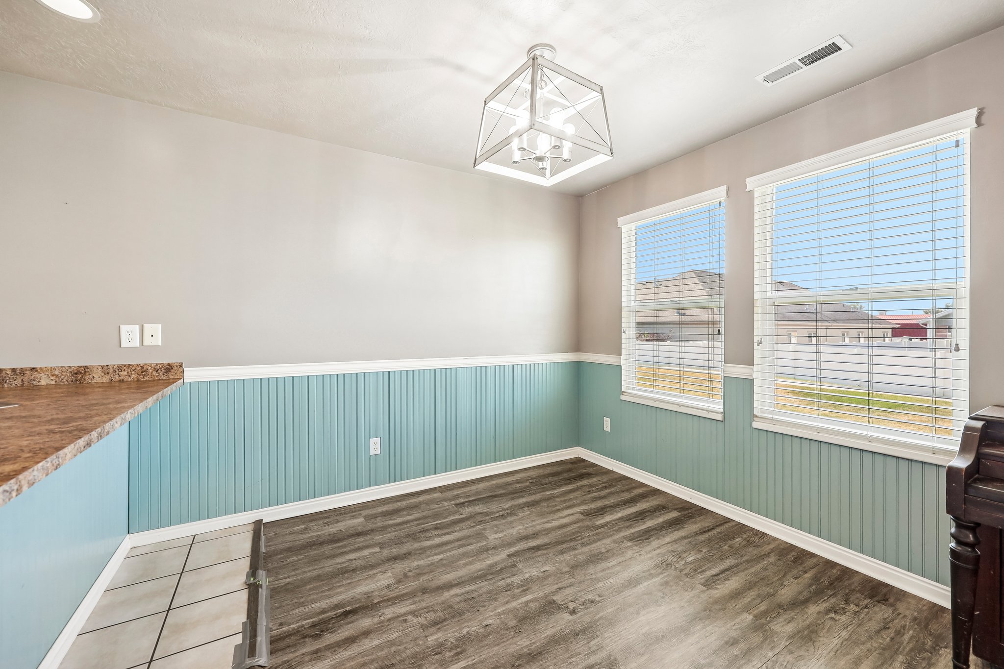 Well-lit room featuring wood-finish flooring, two large windows with blinds, and decorative beadboard wainscoting
