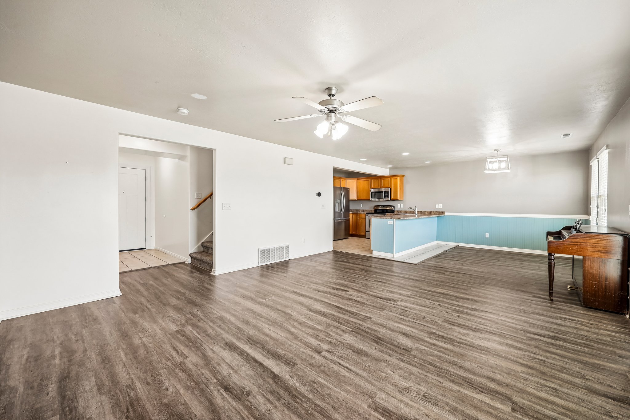 Spacious open-concept living area featuring wood-finish flooring, a ceiling fan with integrated lighting, and neutral wall tones
