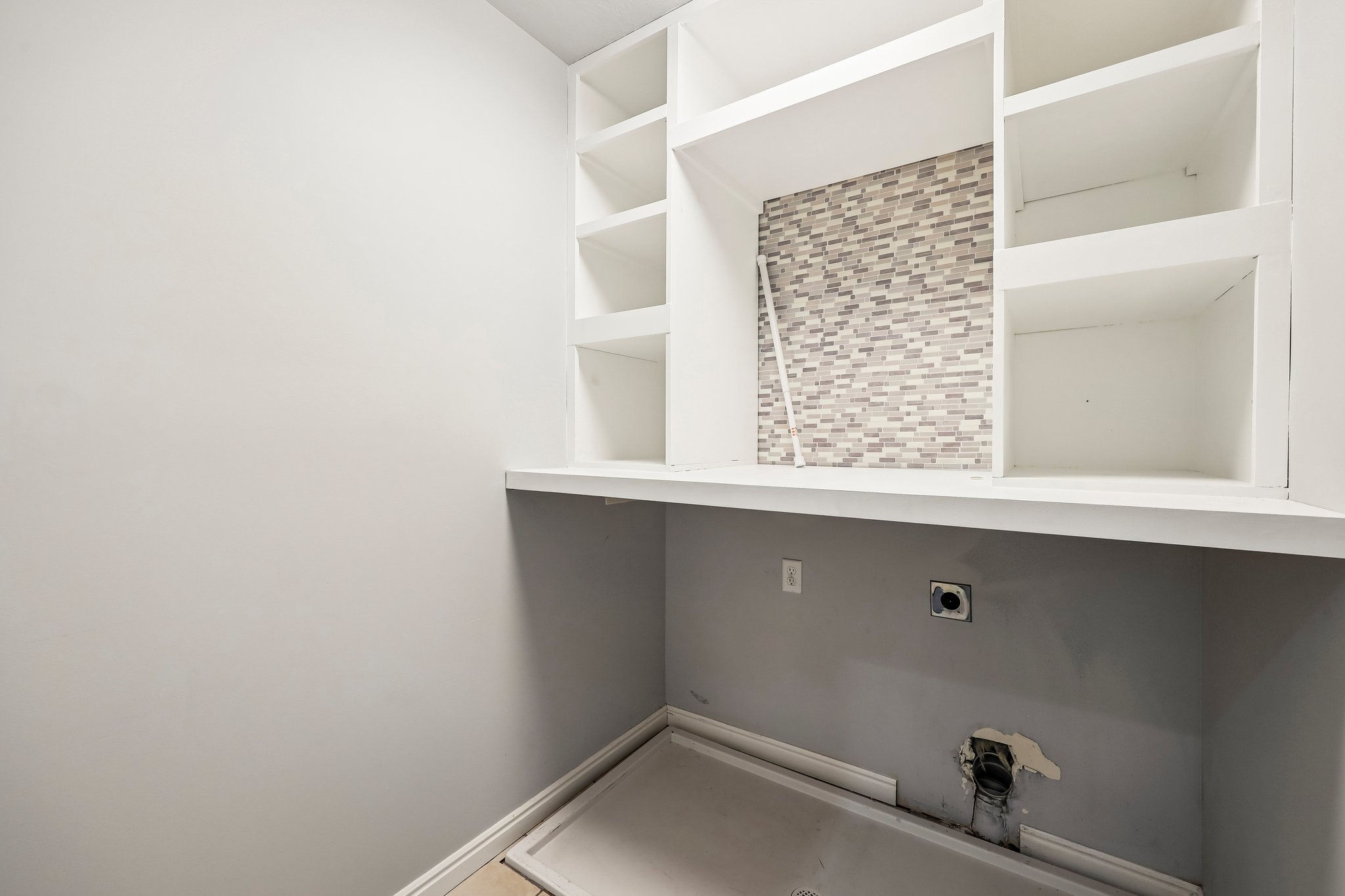 Laundry area featuring a mosaic tile backsplash, built-in shelving, white countertop, and a utility hookup
