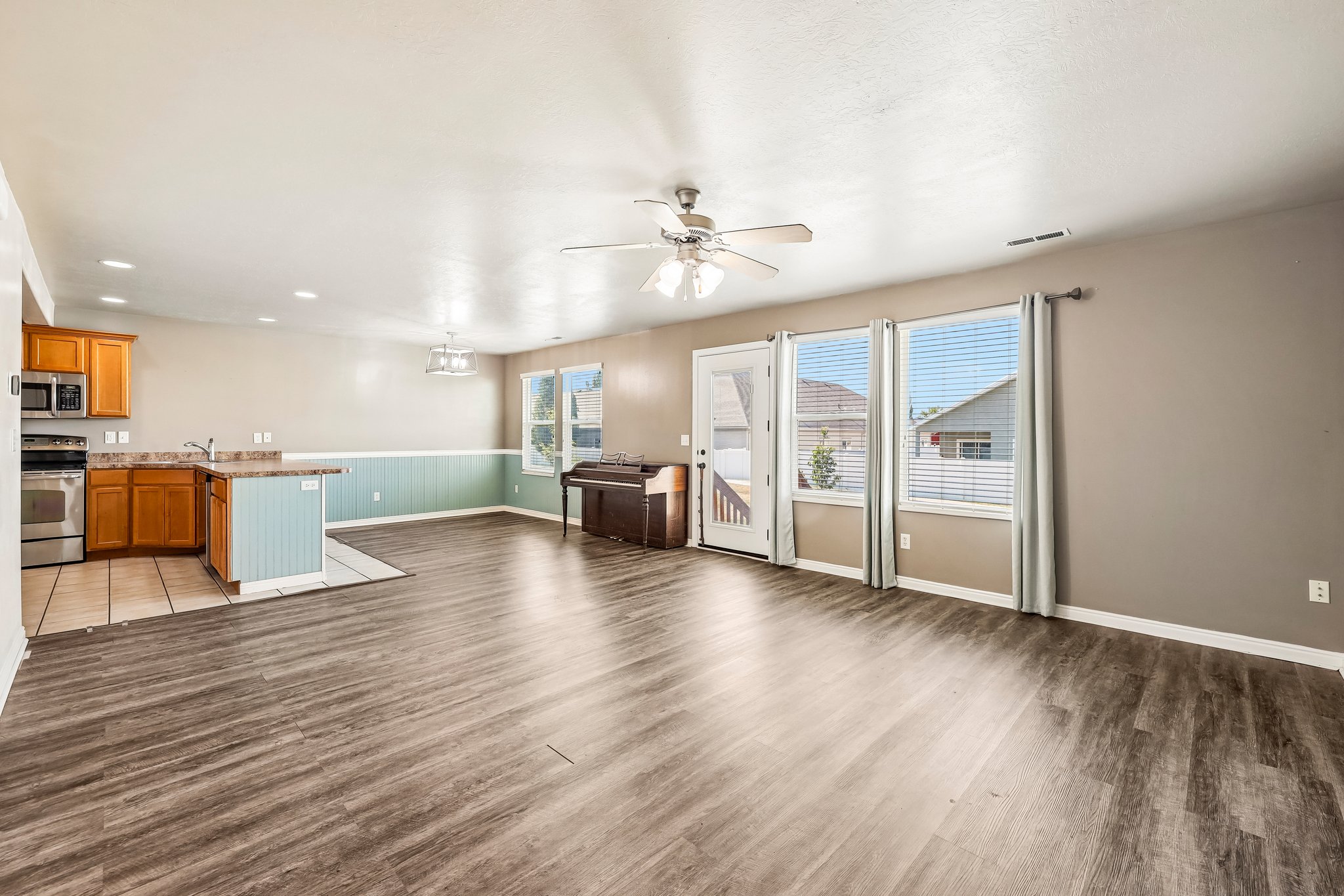 Open-concept living area featuring wood-finish flooring, a ceiling fan, and multiple windows with blinds