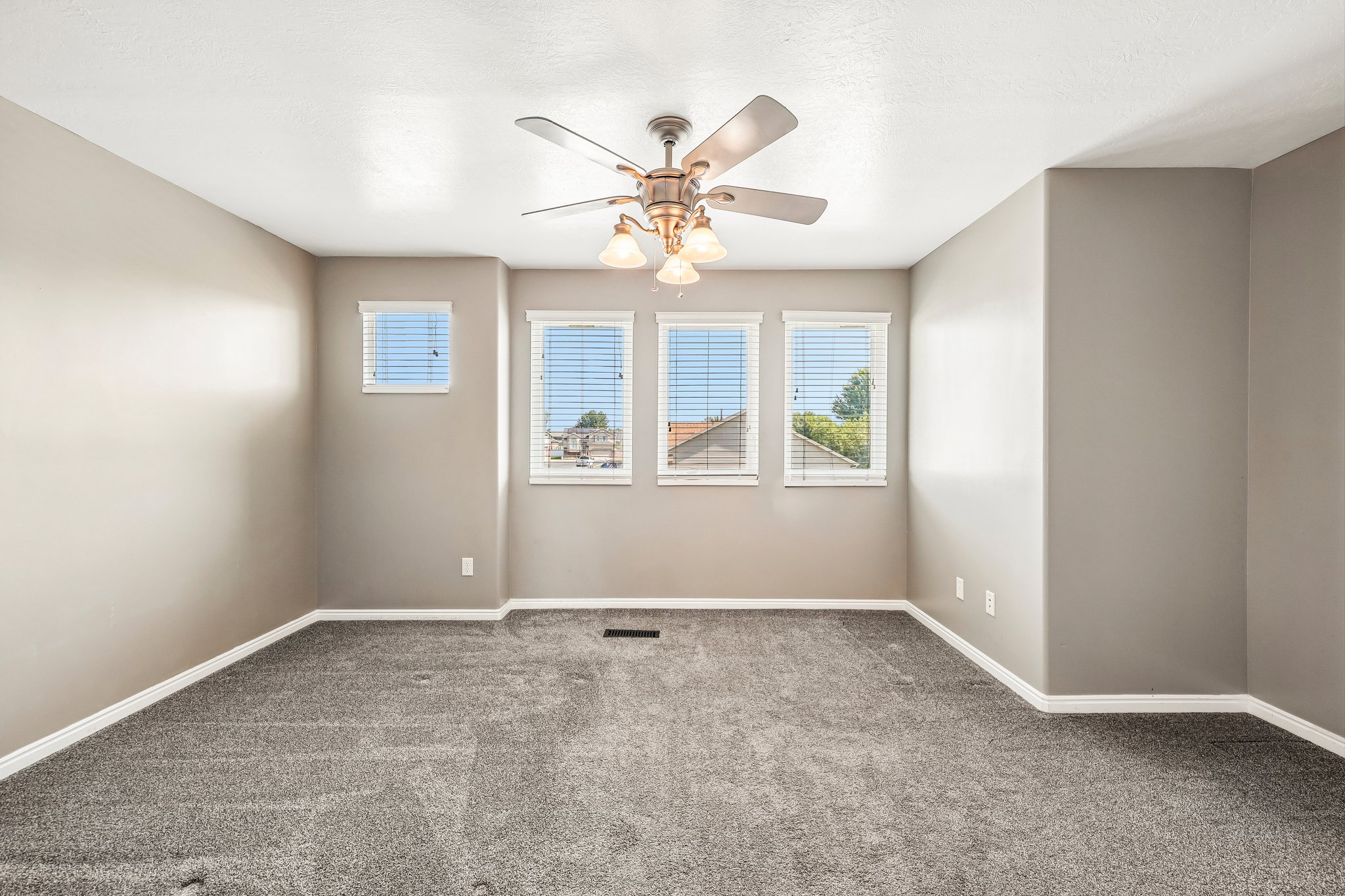 Interior room featuring neutral wall paint, gray carpeting, a ceiling fan with integrated lighting, and multiple windows with horizontal blinds