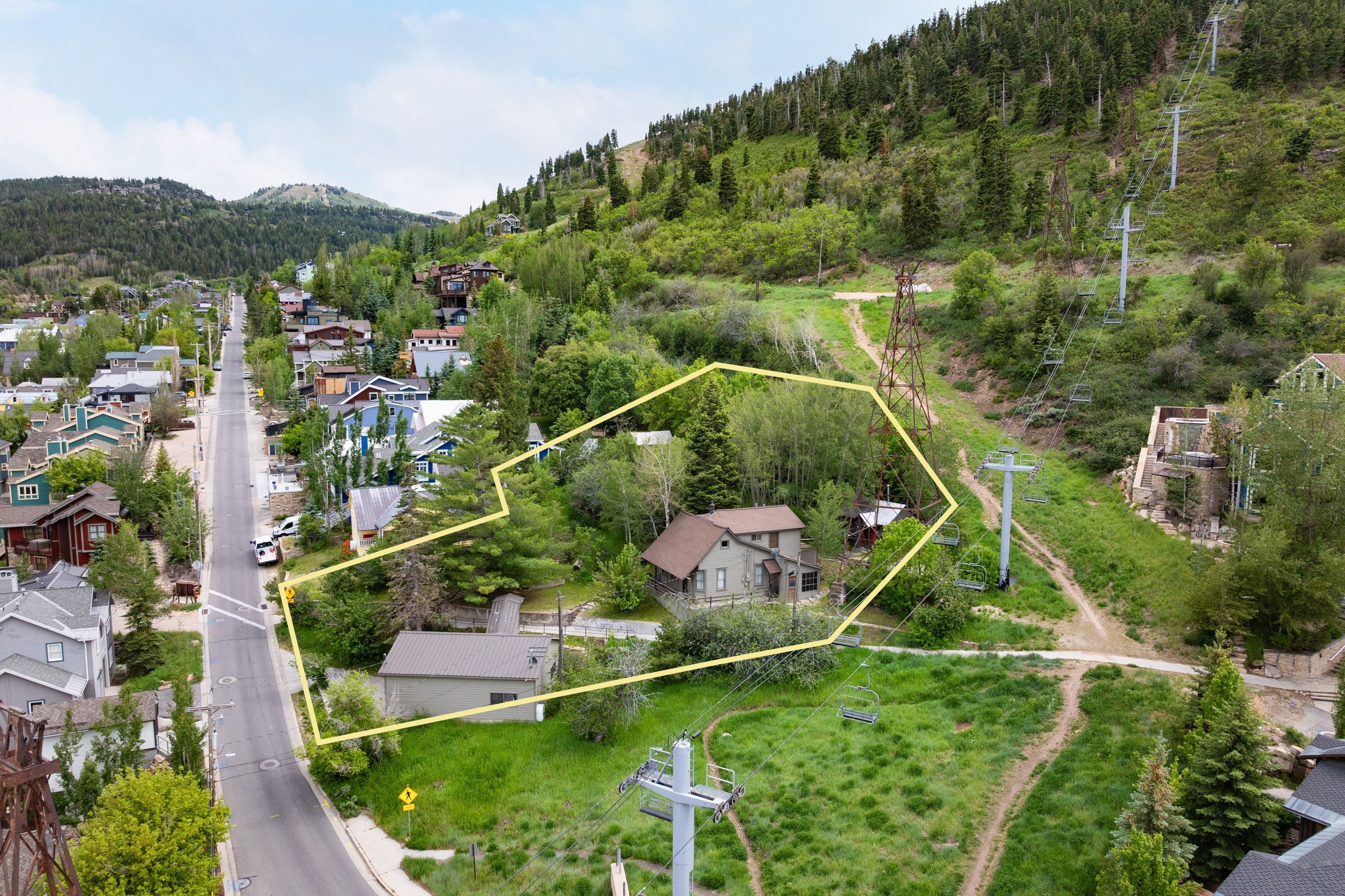 Aerial perspective showcasing a property bordered by a paved road and a wooded hillside