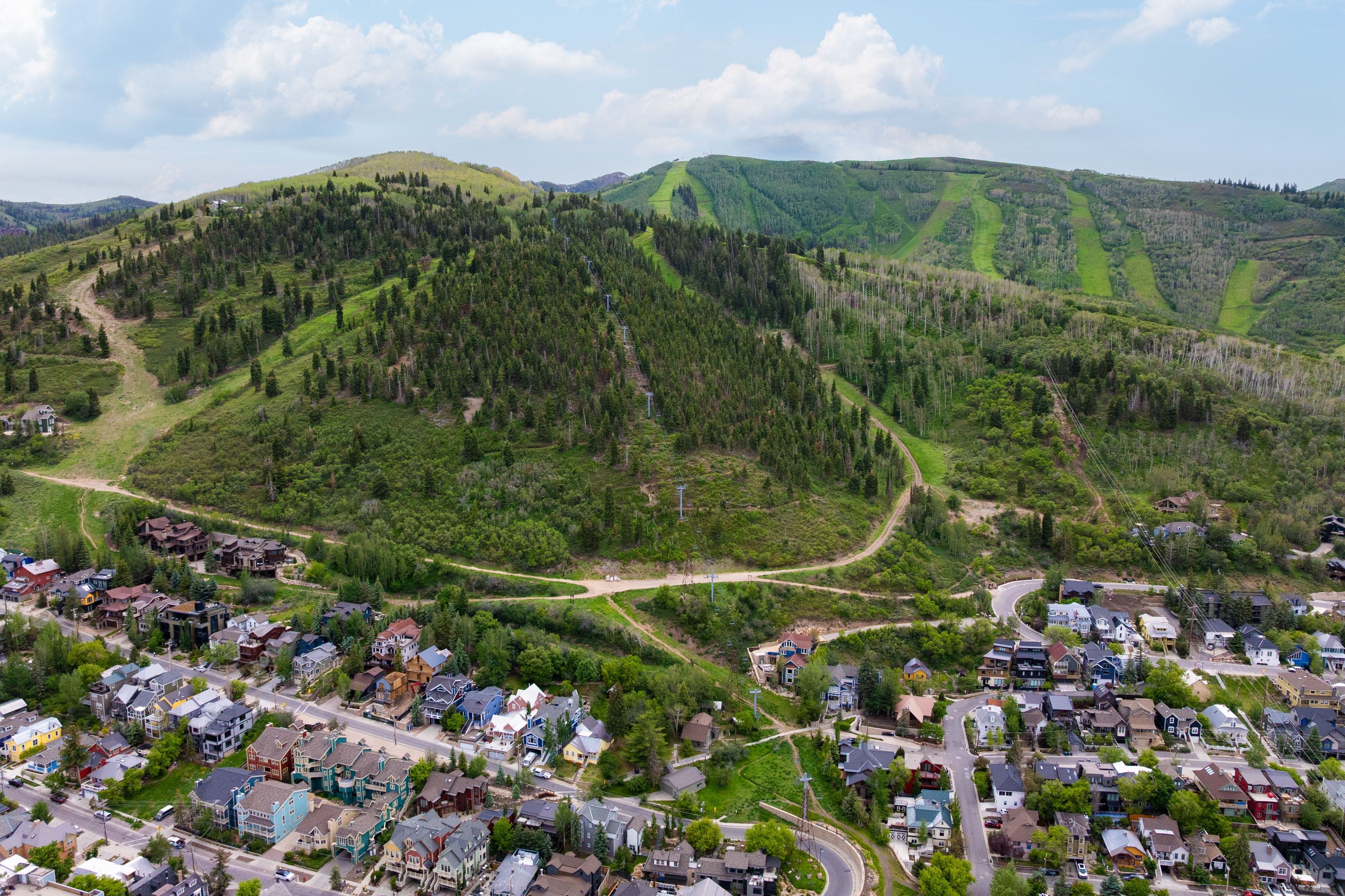 Expansive mountain landscape featuring a residential area with varied housing styles, surrounding dense tree coverage, and visible ski trails on distant hills