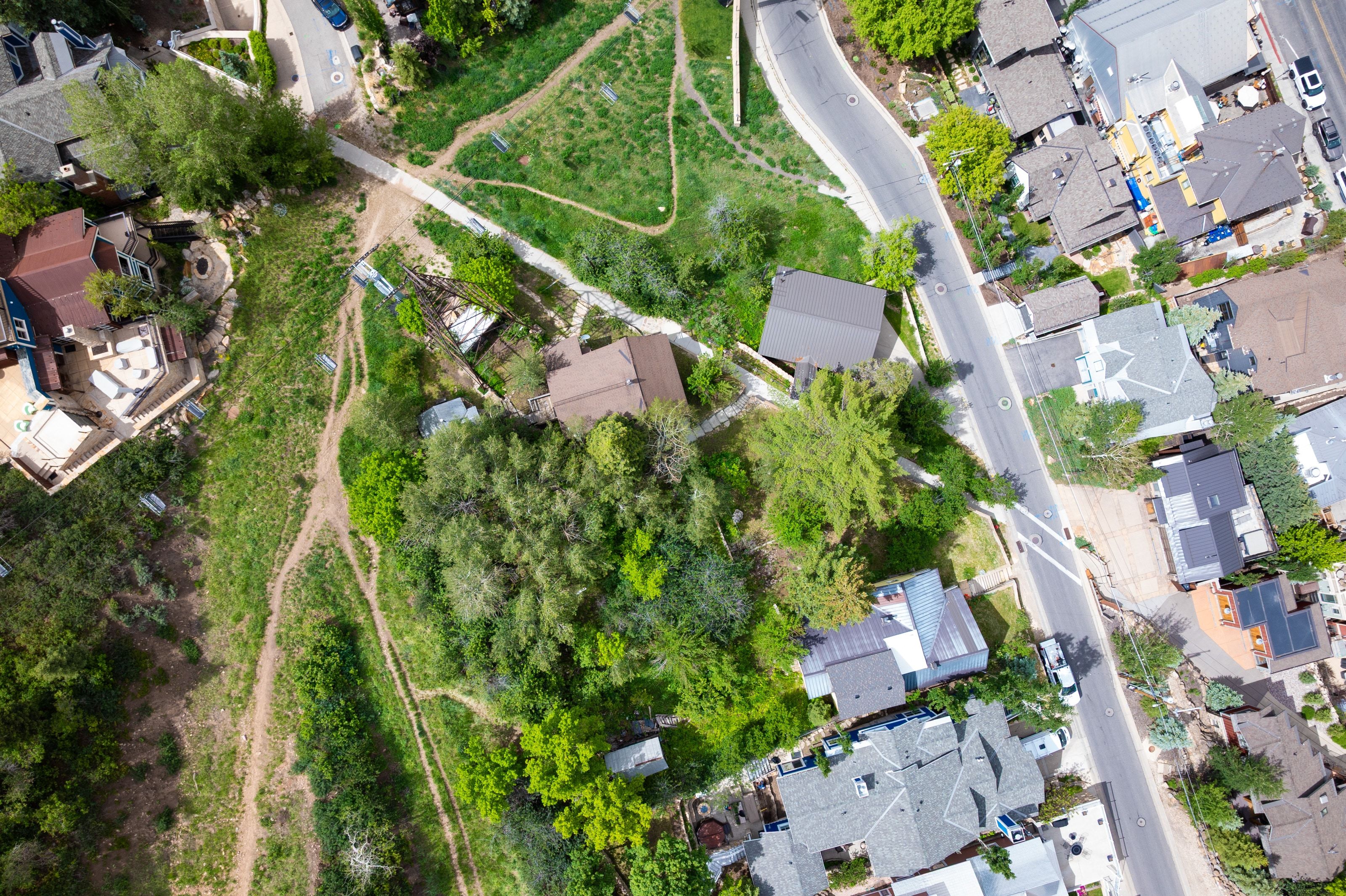 Aerial perspective showcasing a residential area with diverse roofing styles, mature trees, and paved roadways