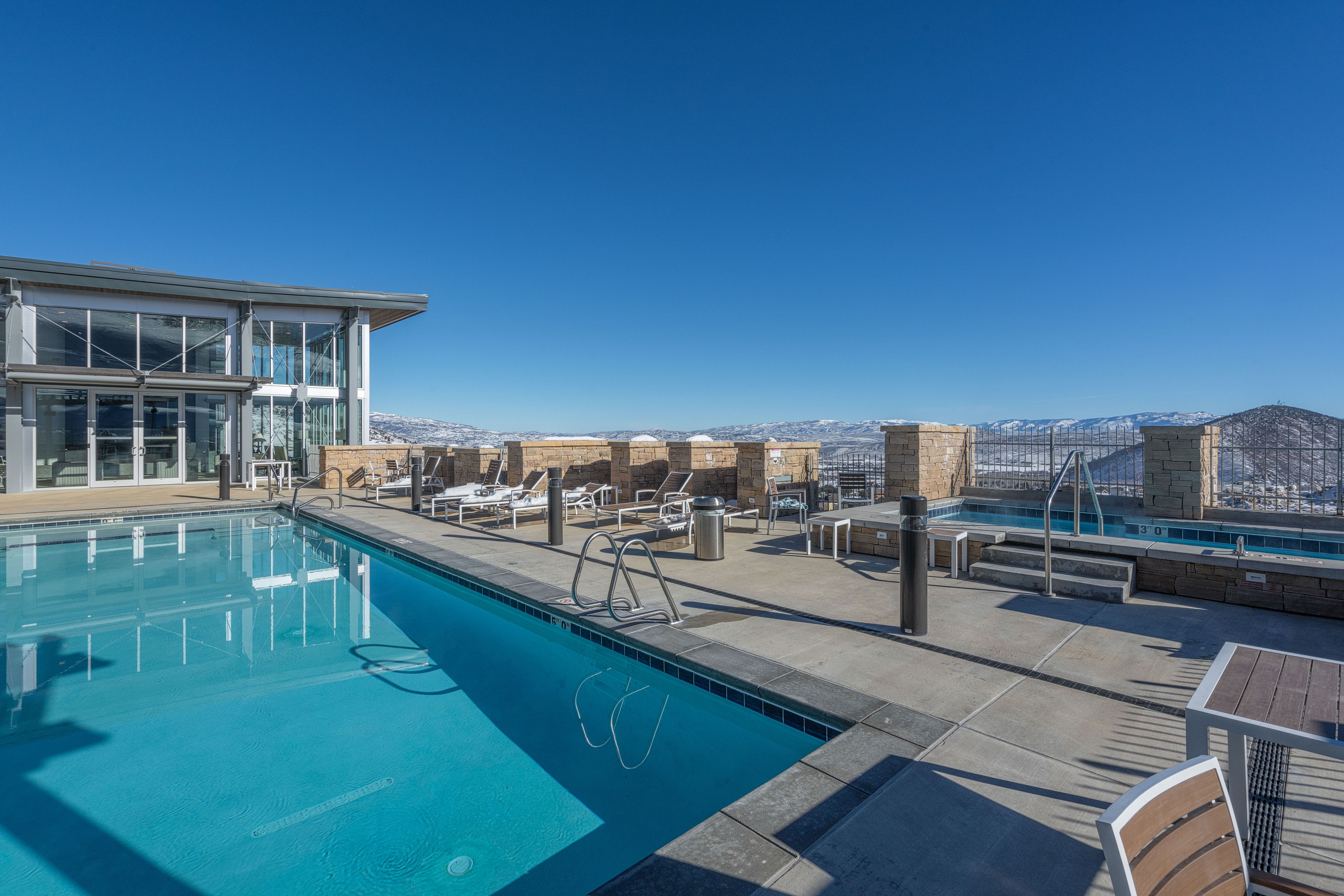 Rooftop amenity space featuring a sparkling swimming pool, integrated hot tub, and expansive concrete decking