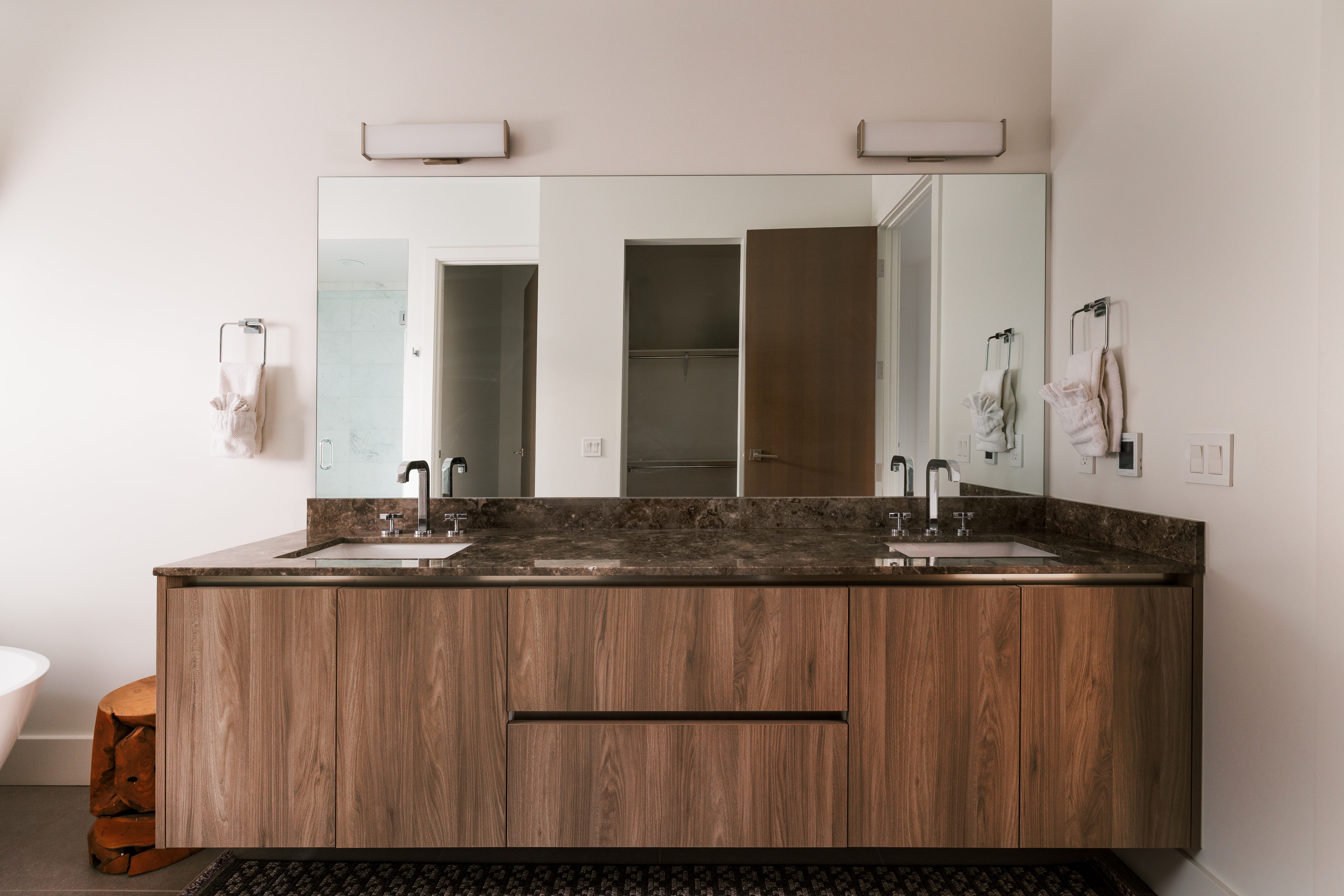Dual vanity with integrated sinks, a dark patterned countertop, wood-finish cabinetry, and an expansive mirror