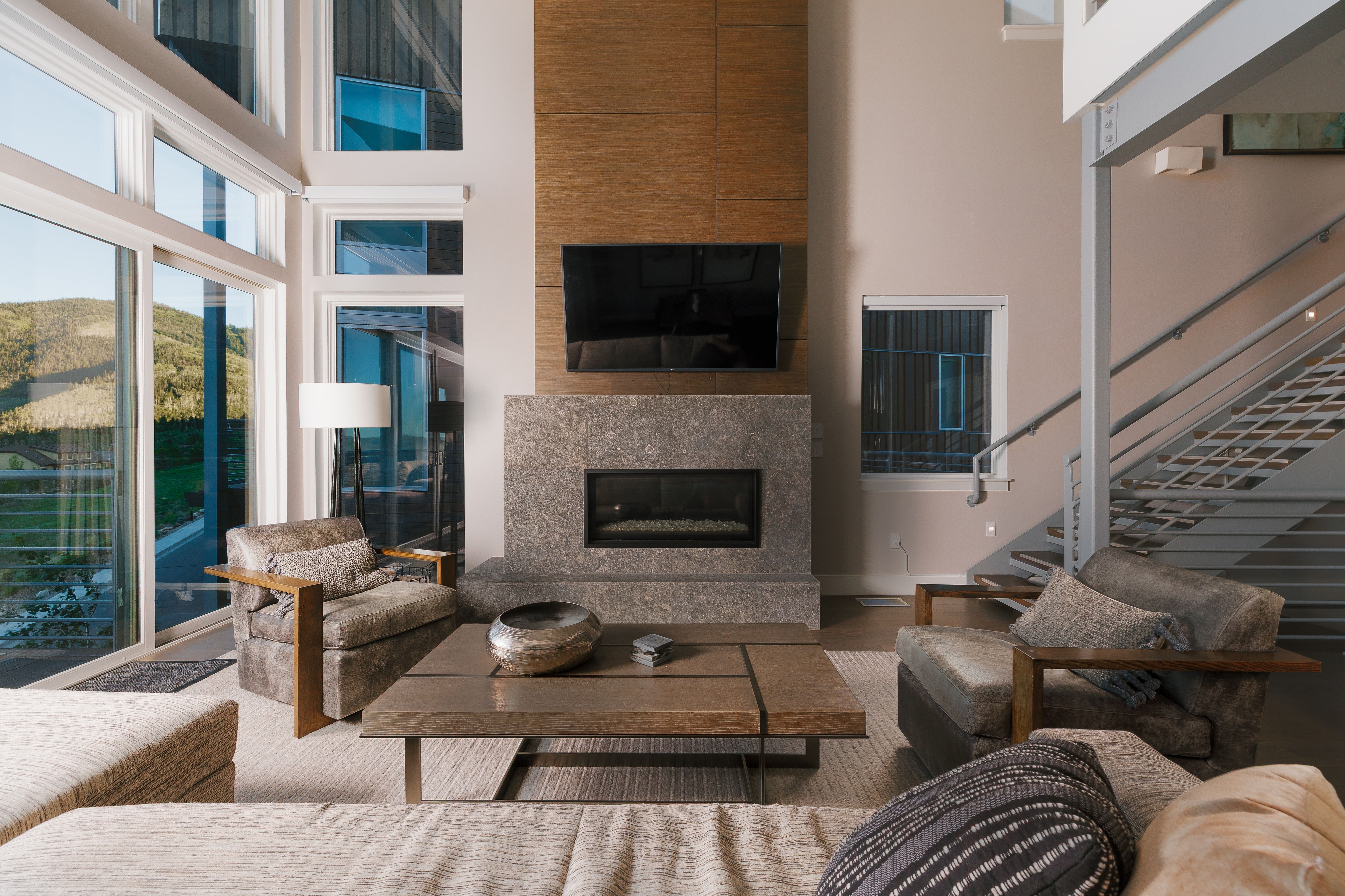 Living area featuring a floor-to-ceiling window wall, a stone-clad fireplace with a wood-finish accent wall, and a multi-level staircase with metal railings