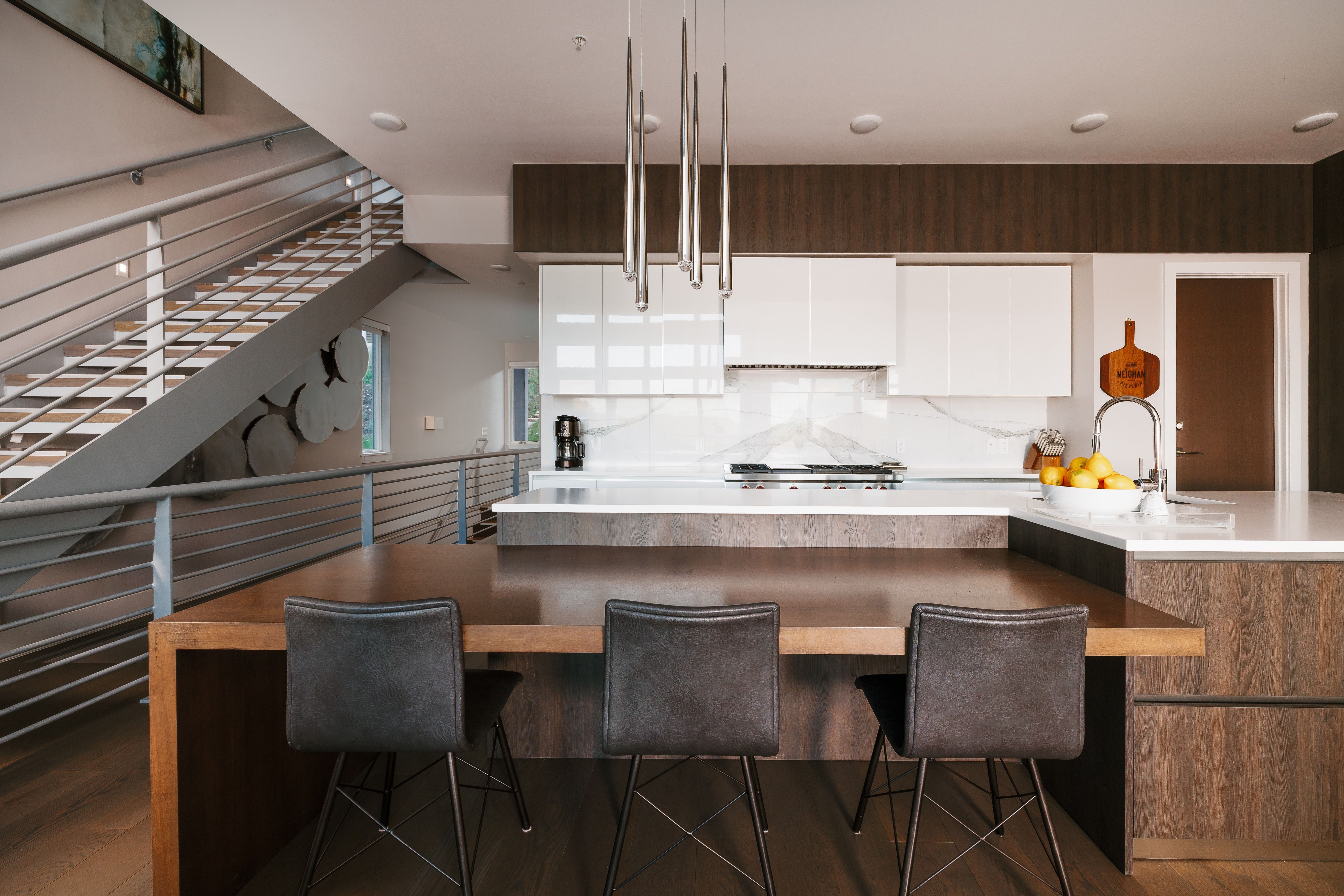 Contemporary kitchen featuring a large island with integrated wood-finish dining surface, white upper cabinetry, and dark wood-finish lower cabinetry