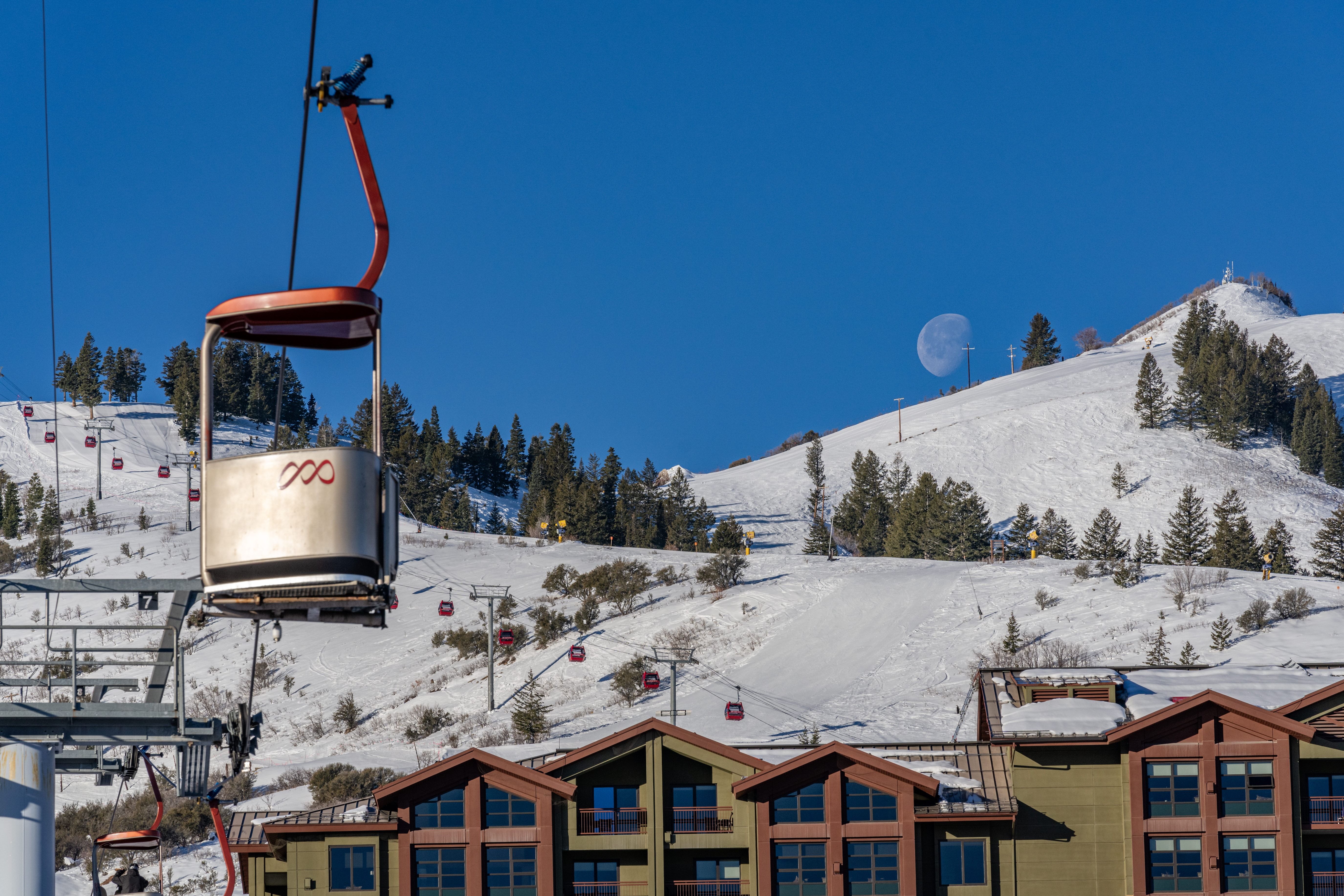 Ski-in/ski-out lodging featuring multi-story buildings with extensive window-work, visible ski slopes, multiple chairlifts, and surrounding mature evergreens