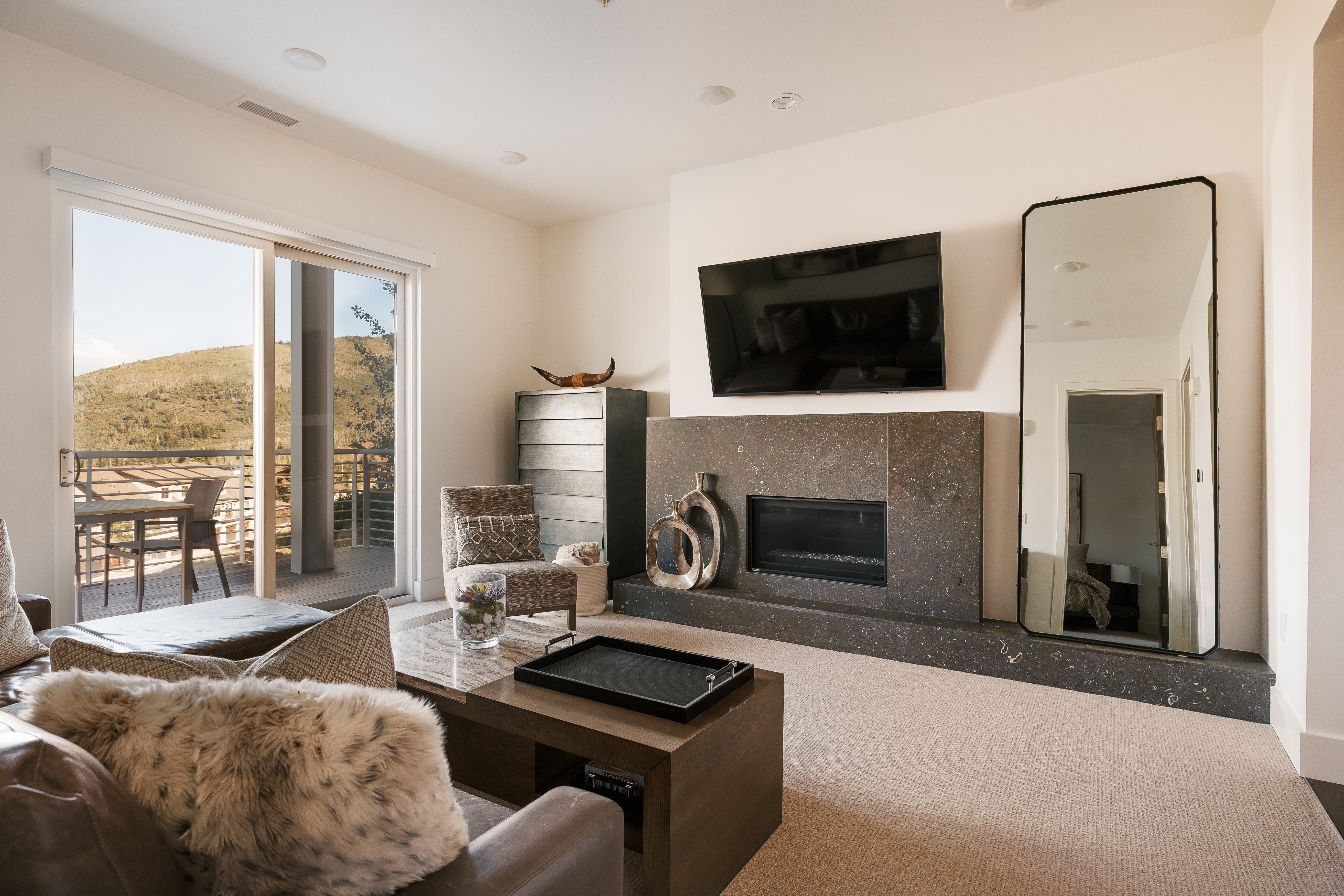 Spacious living area featuring a built-in fireplace with a stone surround and hearth, neutral carpet flooring, recessed lighting, and a sliding glass door opening to an outdoor patio with mountain scenery